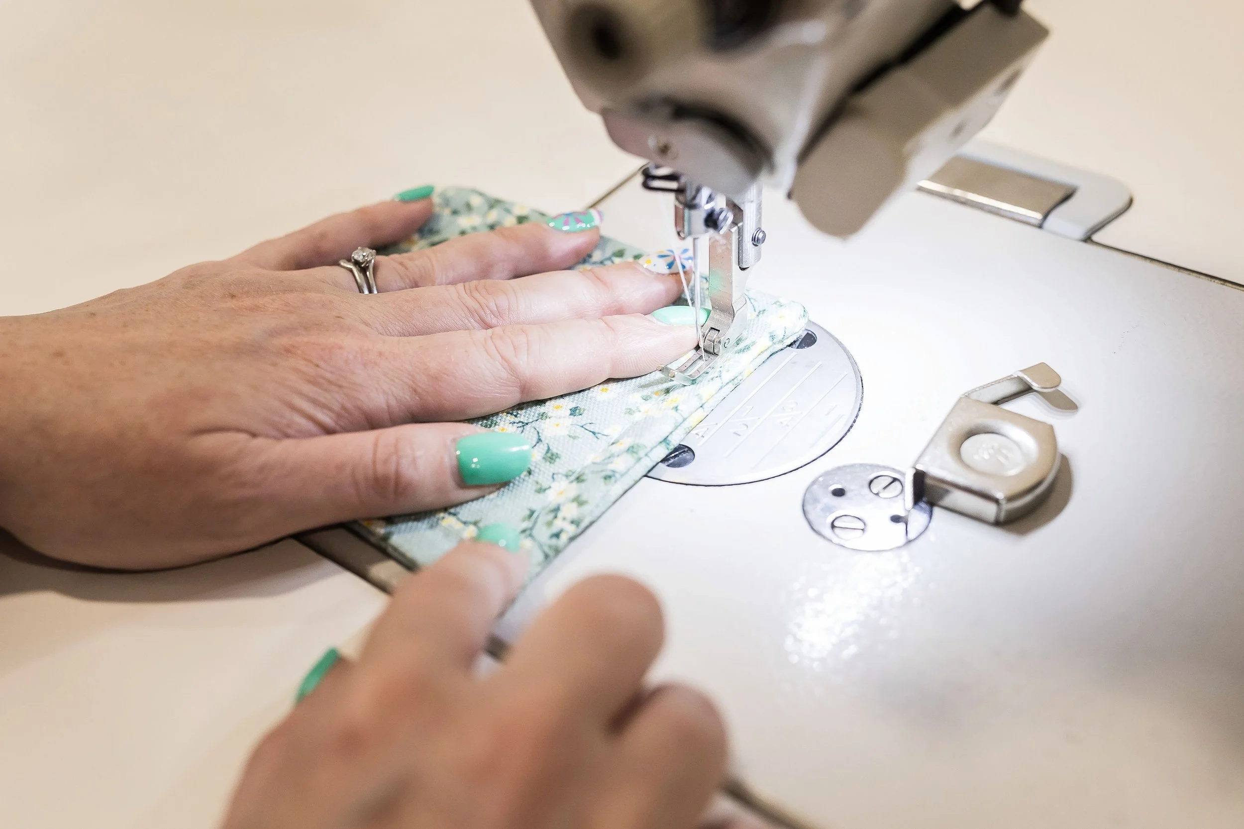 Close-up of hands guiding floral fabric through a sewing machine