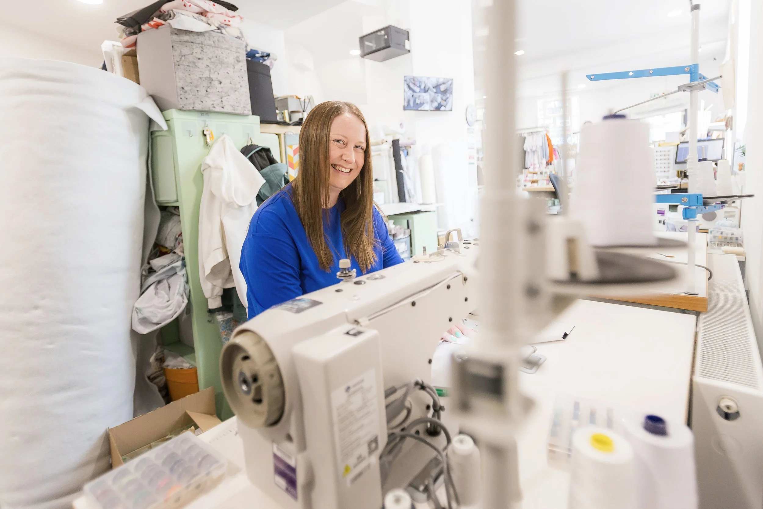 Kirsty smiling behind an industrial sewing machine in the shop's workroom
