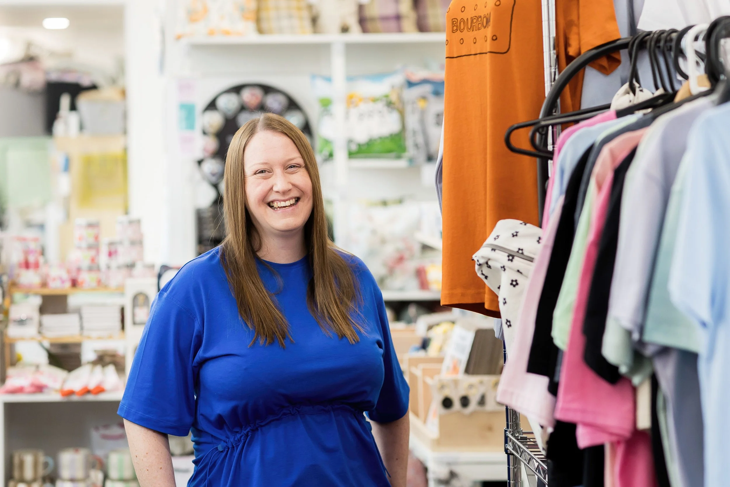 Portrait of Kirsty beside clothing rails in her shop