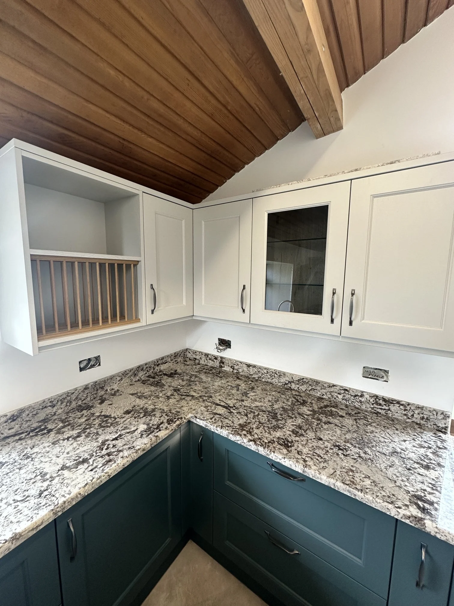 Kitchen with white upper cabinets, teal lower cabinets, granite countertops, and wooden ceiling.