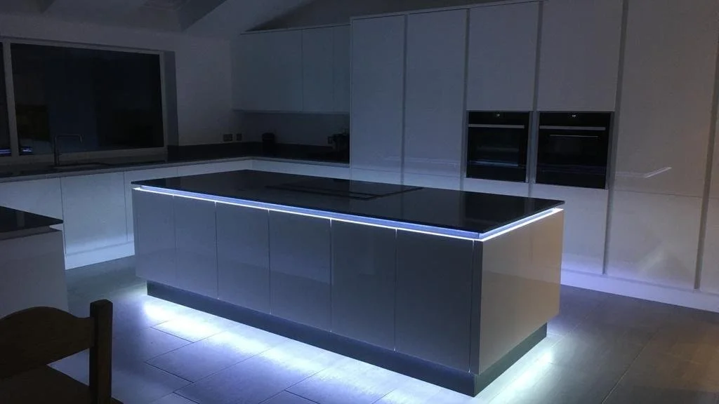 Modern kitchen with white cabinets, black countertop island with LED lighting, dark appliances, and a window at the back.
