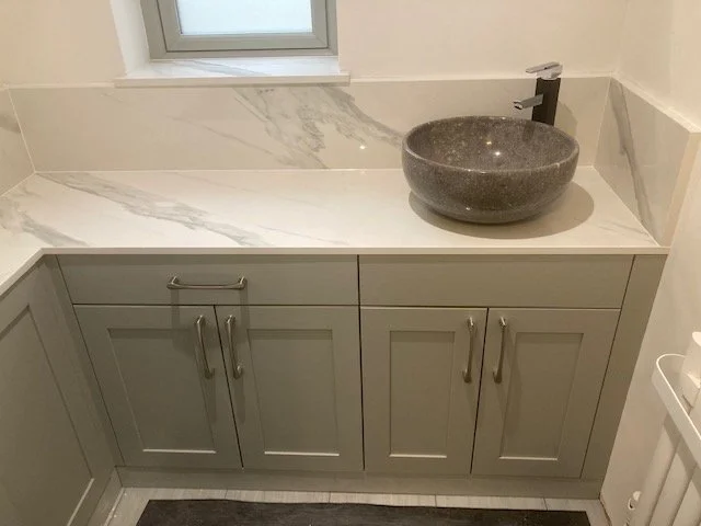 Bathroom vanity with gray cabinet doors, a white marble countertop with gray veining, a stone vessel sink, and a modern black faucet. A small window is above the vanity.