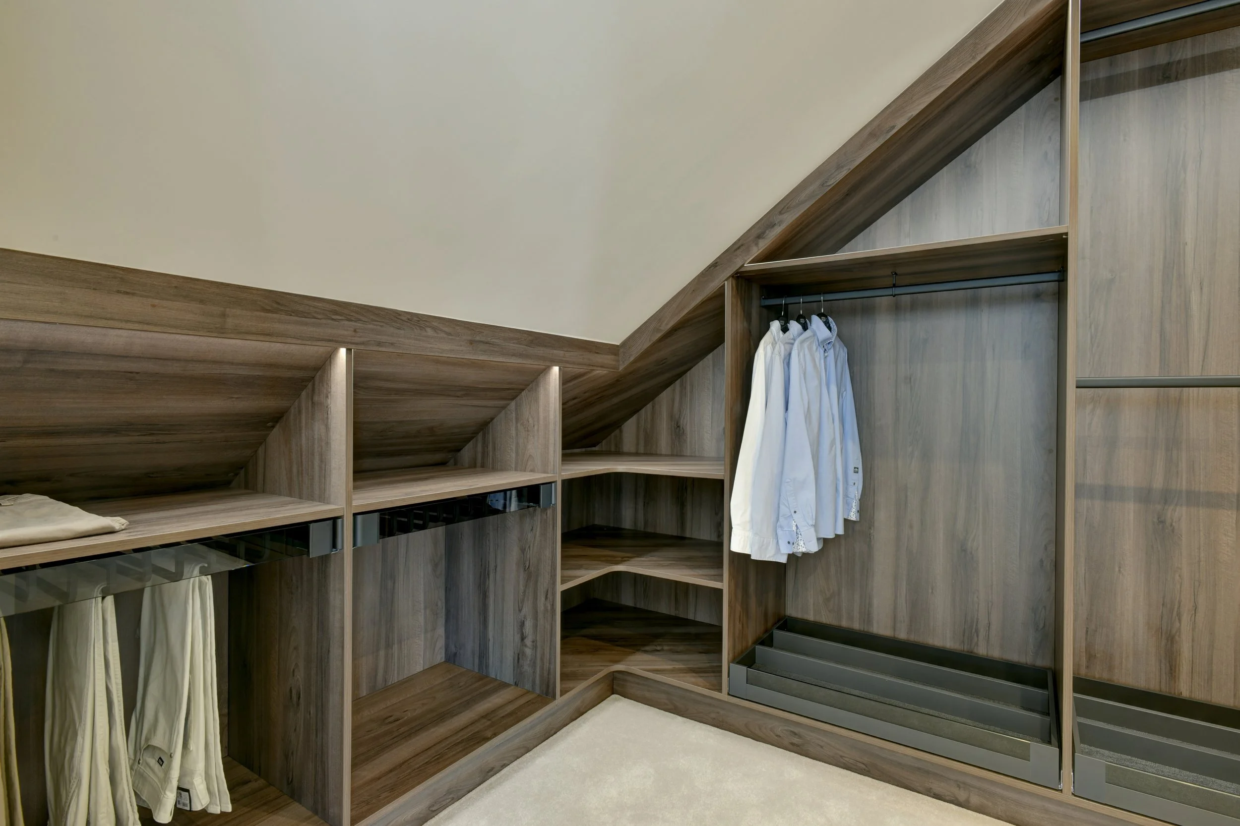 Walnut walk-in closet with wooden shelves and hanging clothes. 