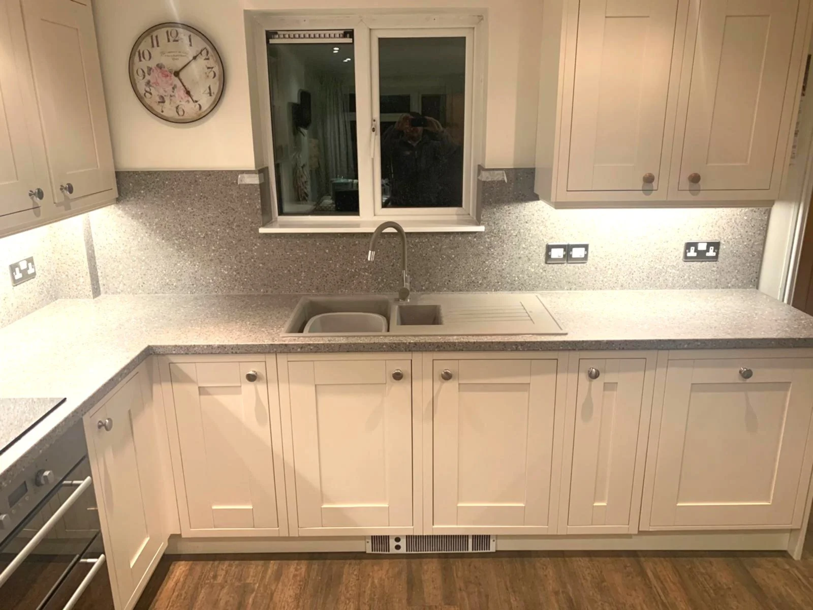 A modern kitchen with off white cabinets, a speckled countertop, and a window above the sink.