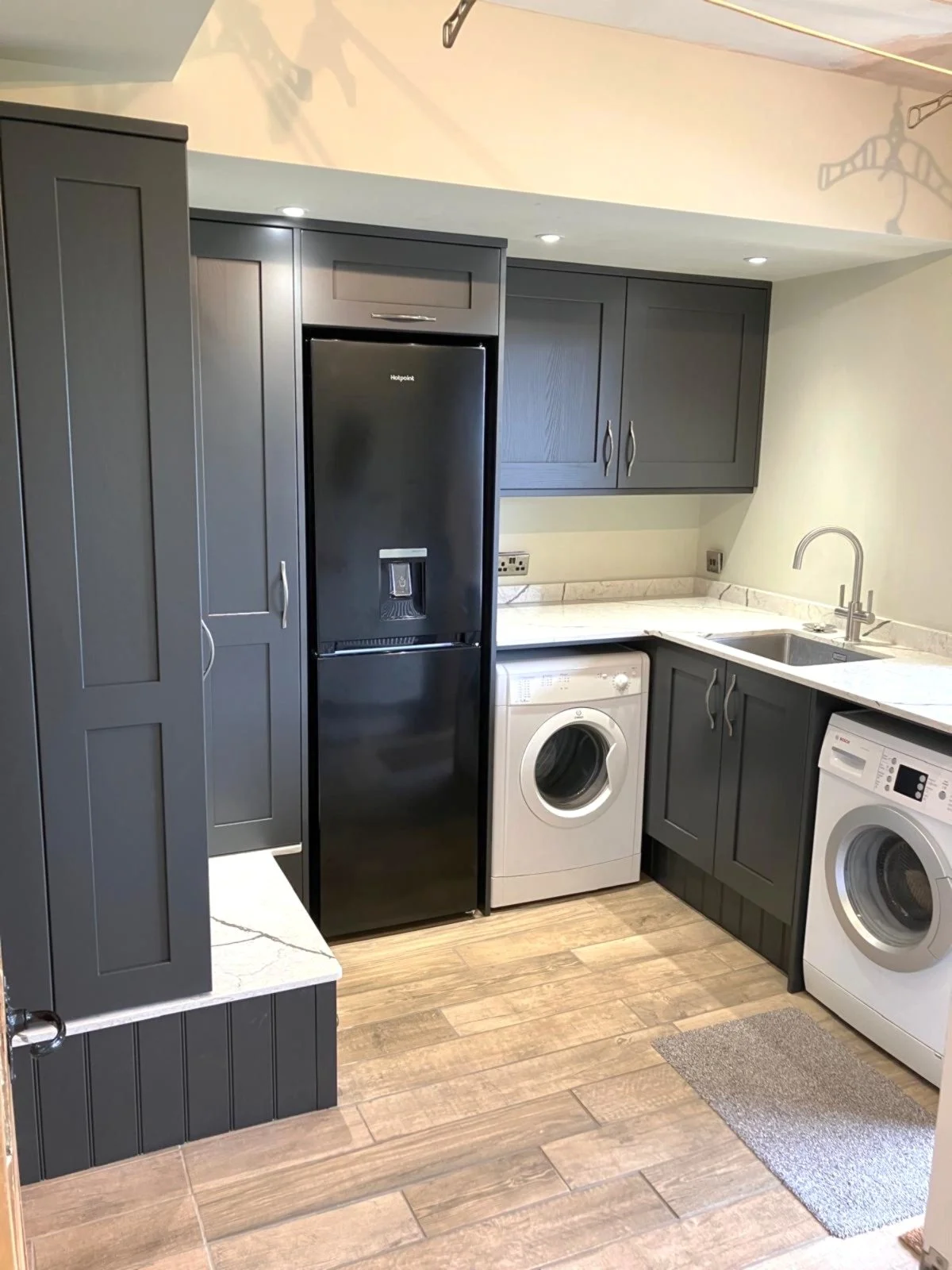 Kitchen with grey cabinets, a black refrigerator, a white washing machine, a white dryer, a marble countertop, and a stainless steel sink.