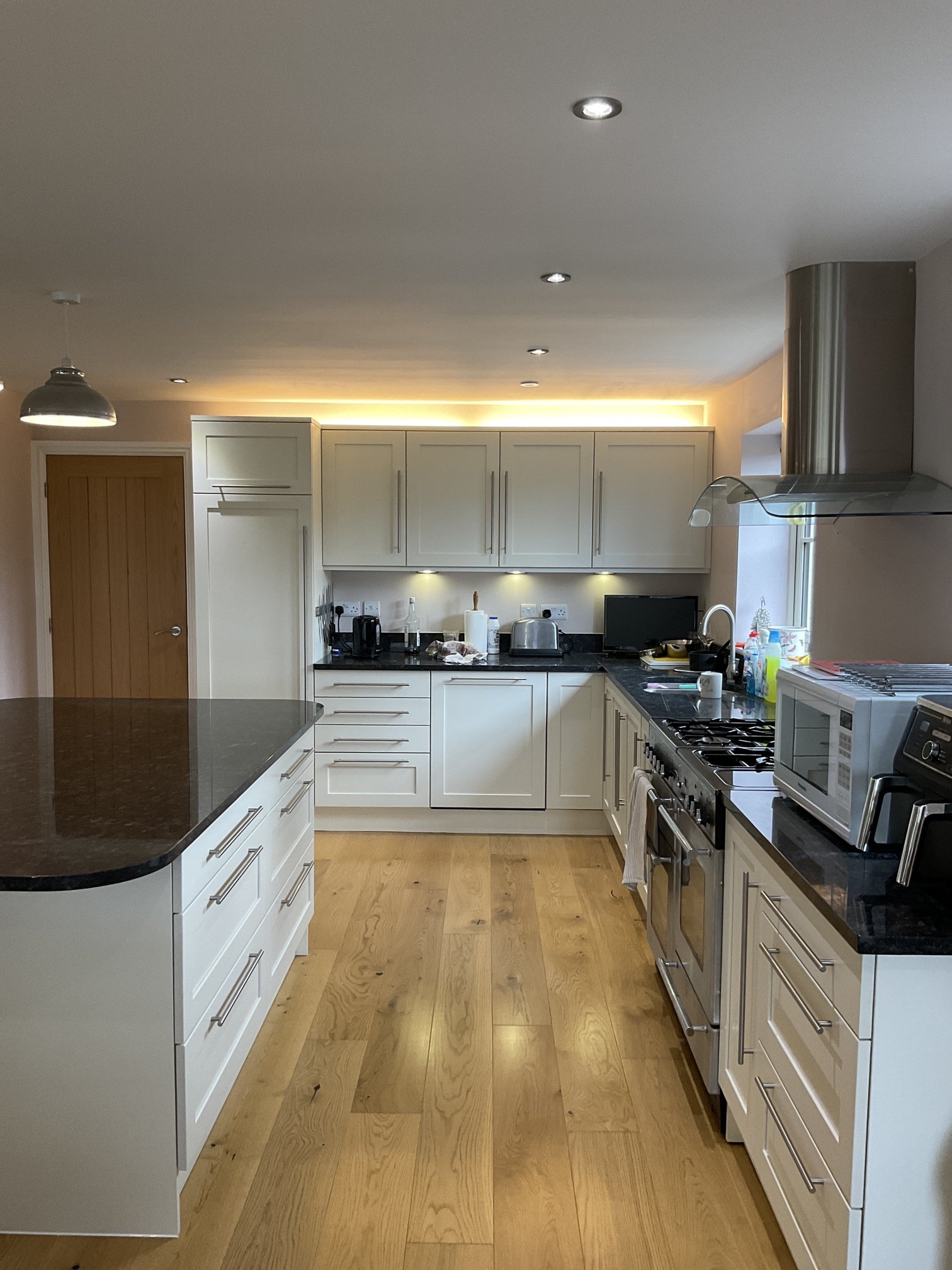 Modern kitchen with white cabinets, black countertops, stainless steel appliances, light wood floors, and a ceiling with recessed lighting.