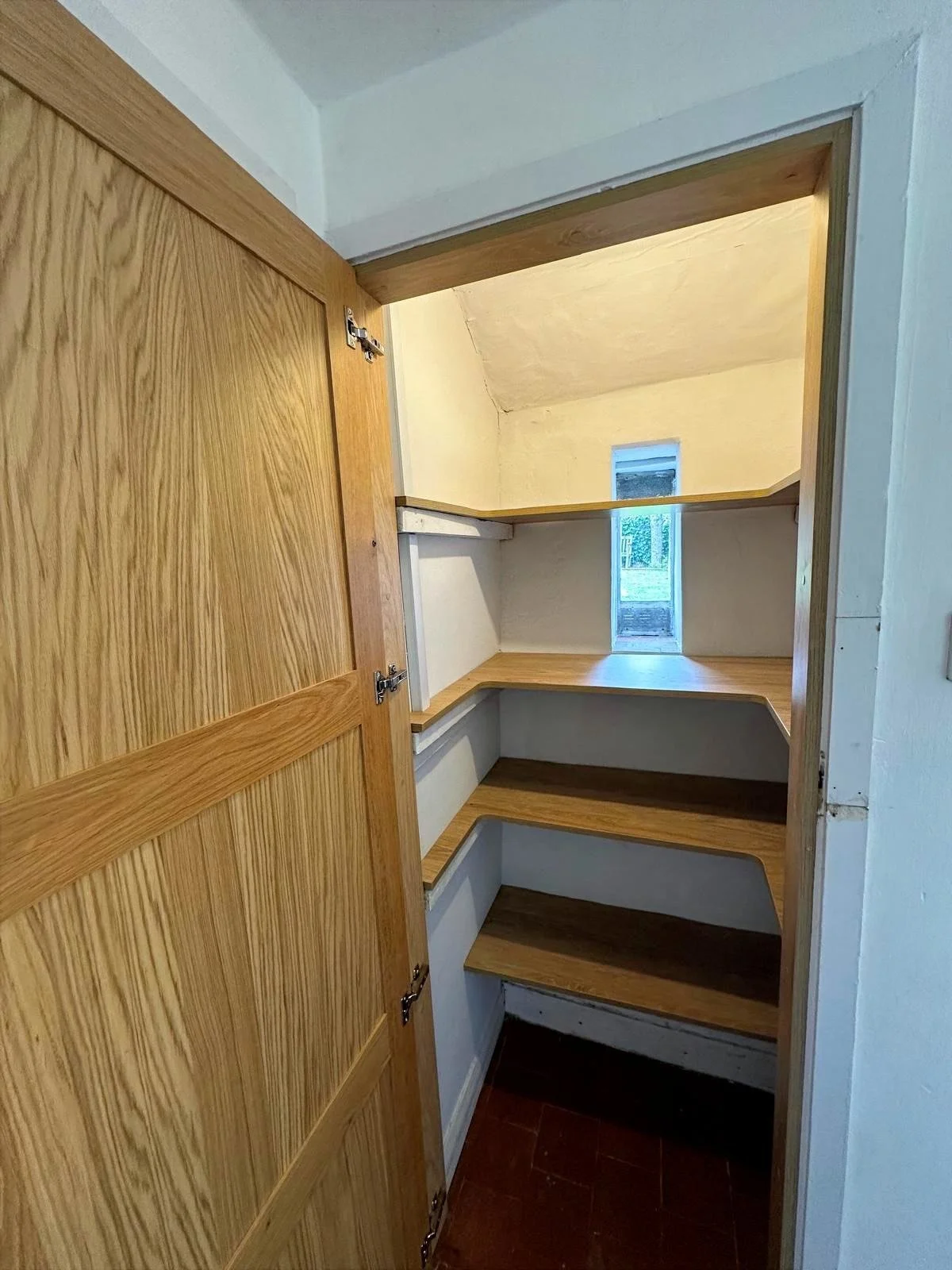 Interior of a small closet with wooden shelves and a small window at the back.