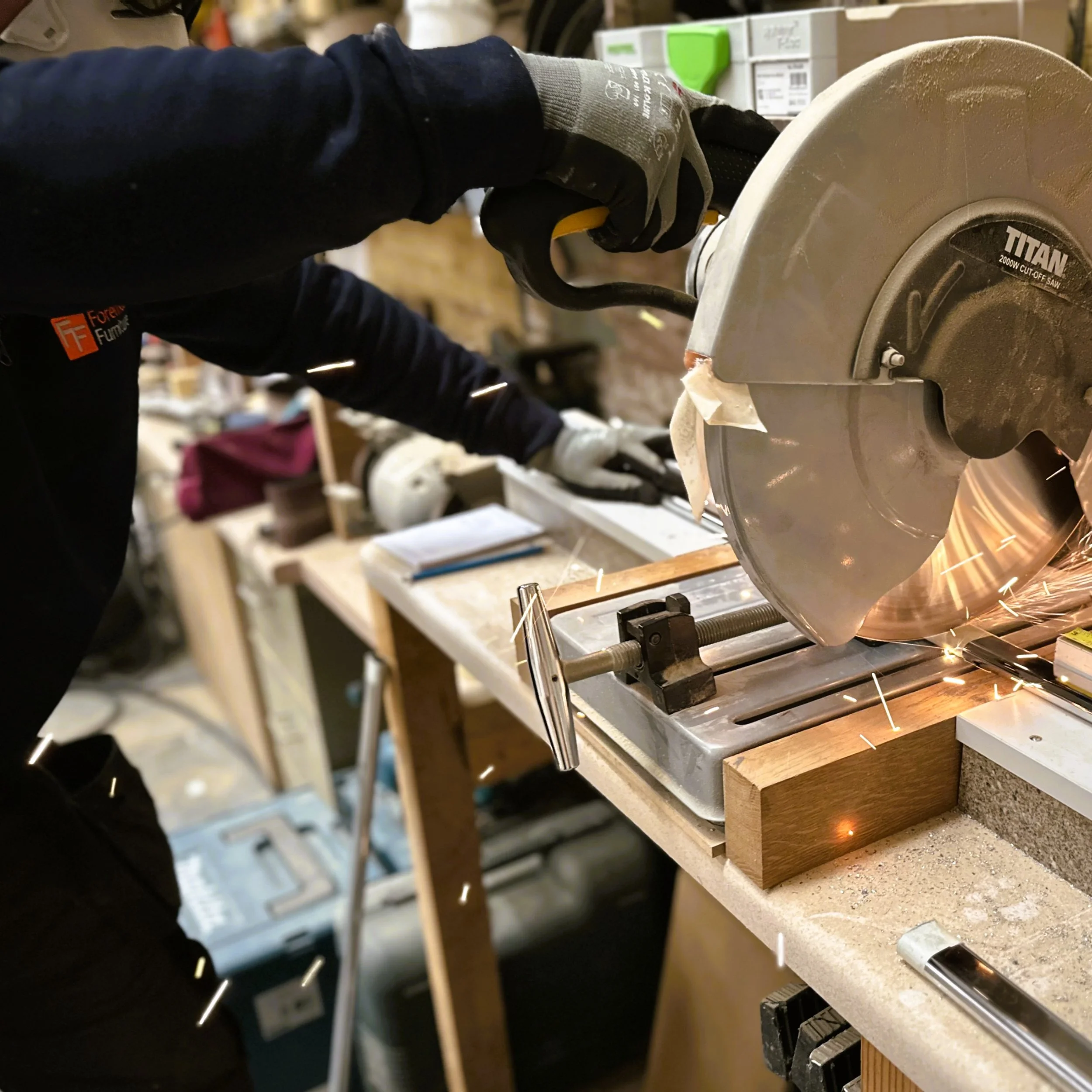 Person wearing gloves and using a saw to cut a piece of metal in a workshop.