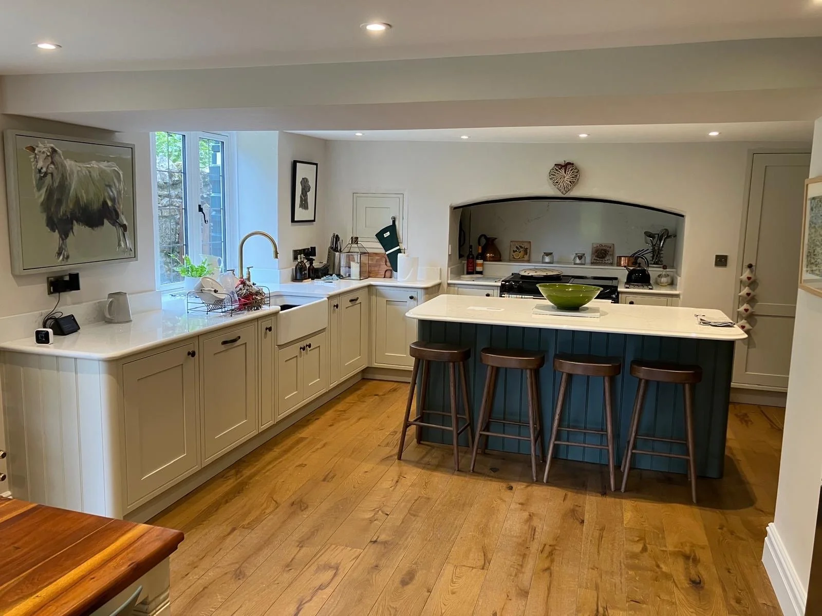 A traditional kitchen with white cabinets, a blue island with a white countertop, wooden stools, a window with a view of trees, and various kitchen appliances and decor.