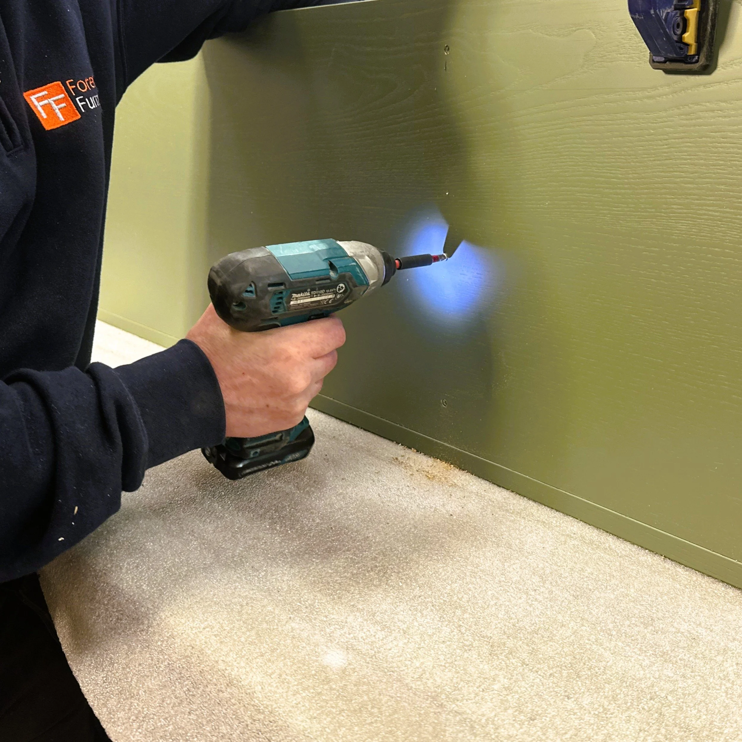 Person holding a cordless power drill with a bit attached, drilling into a green cupboard.