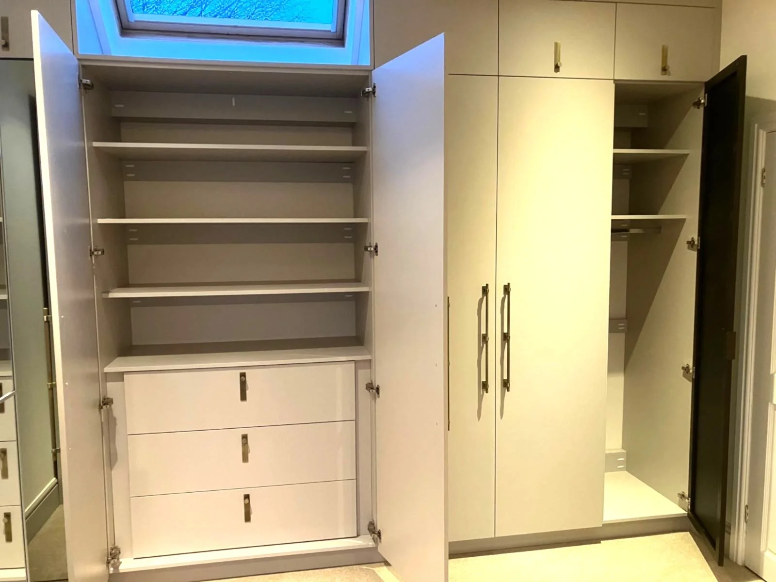 Open wardrobe cabinets with shelves and drawers shown in a room with a small window above.