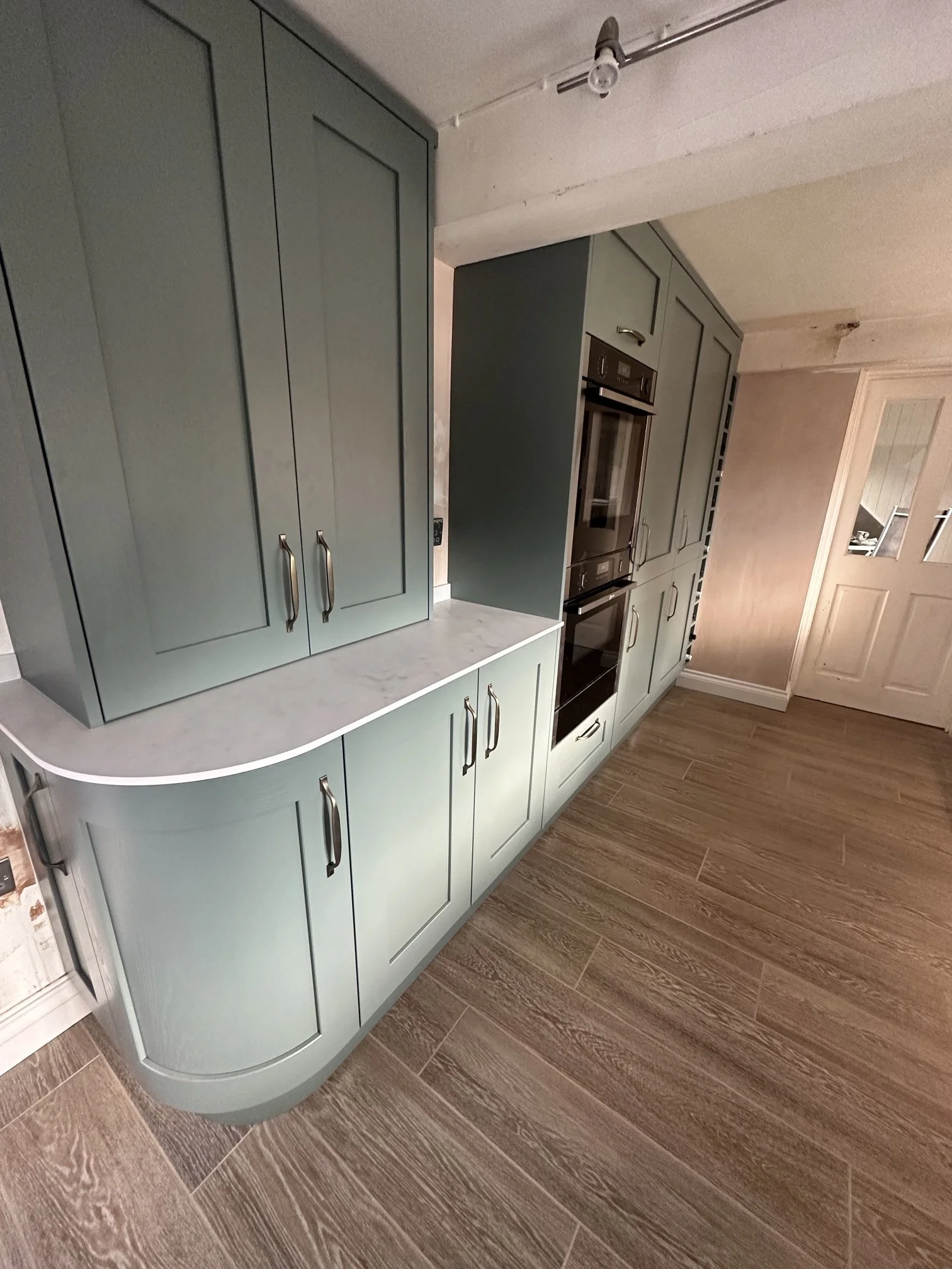 Kitchen with green cabinets, a built-in oven, marble countertop, and wooden floor.
