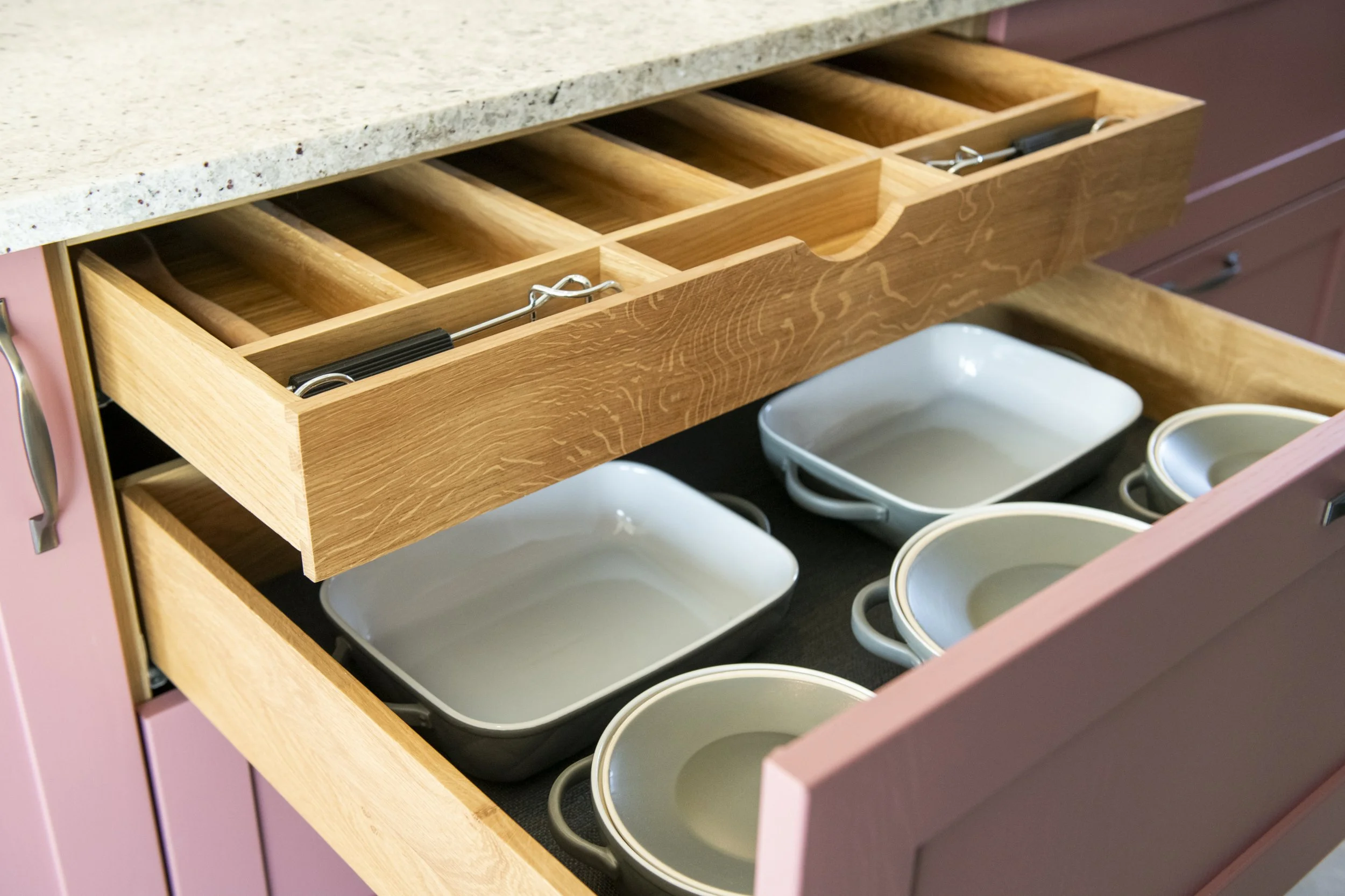 Open kitchen drawer with wooden divider and white bowls inside.