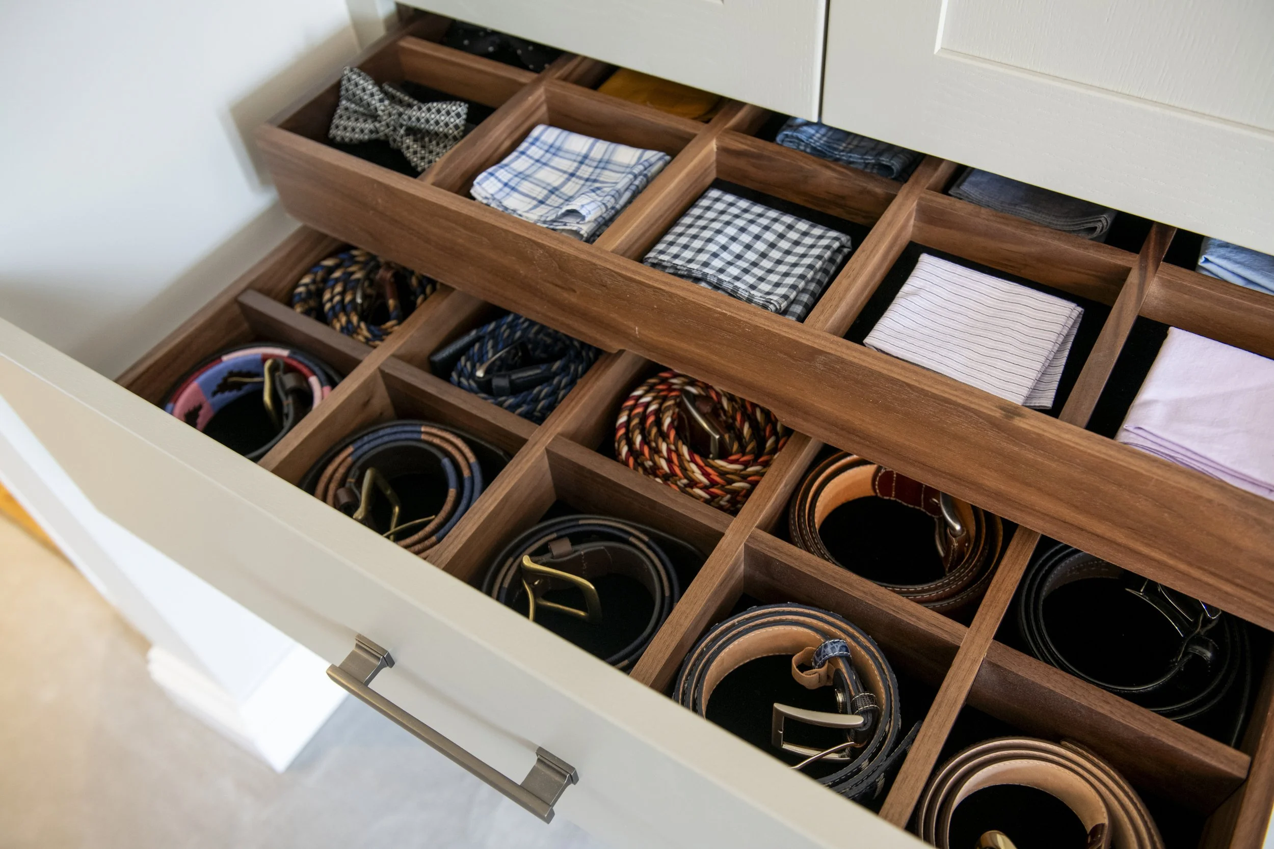 Wardrobe walnut drawer with compartments filled with neatly folded belts, and accessories.