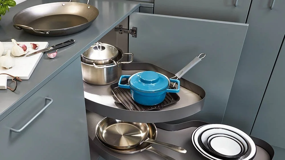 Vauth-Sagel corner unit shown in kitchen corner with stacked plates, a blue cast iron pot and a stainless steel saucepan.