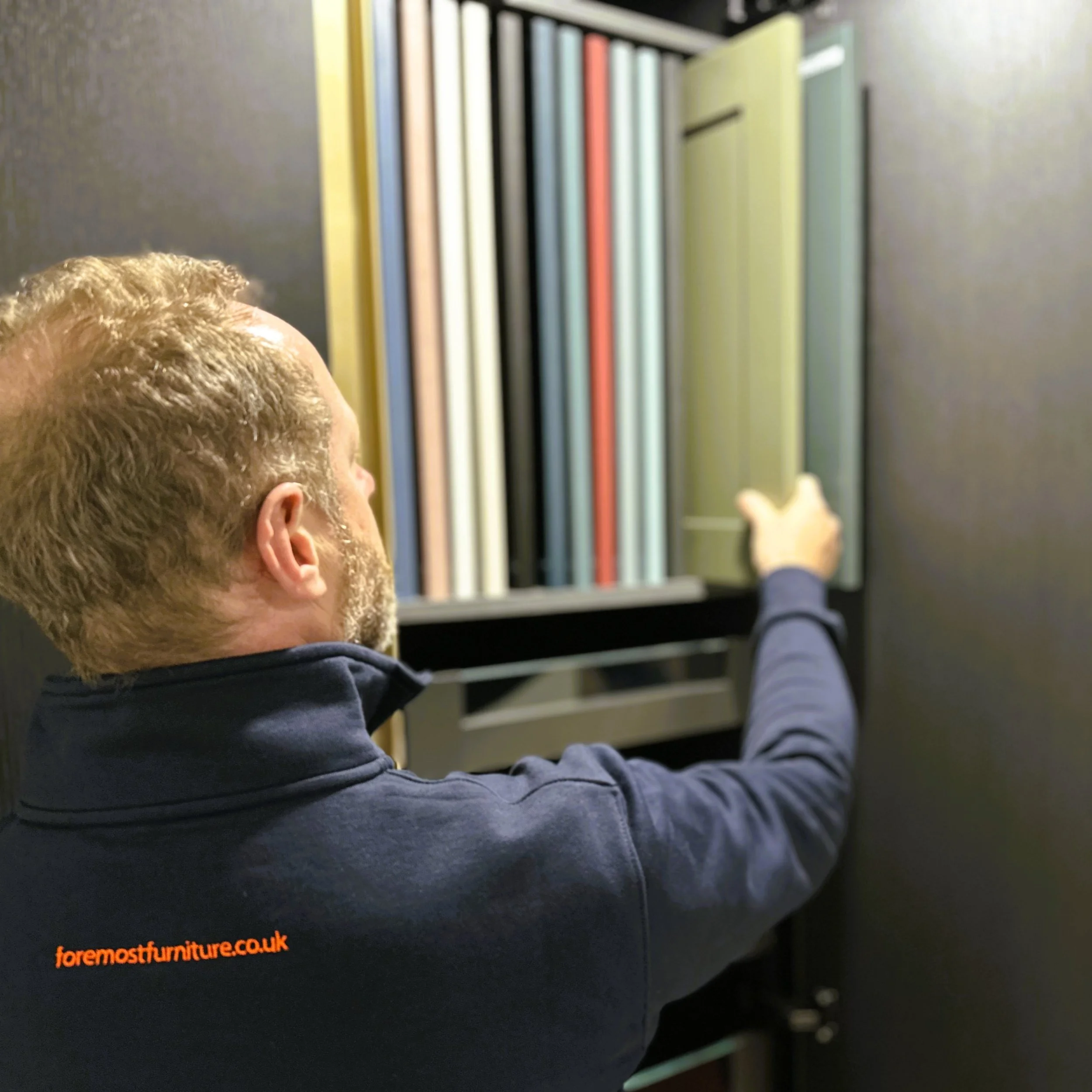 A person showing a row of colorful door samples on a shelf.
