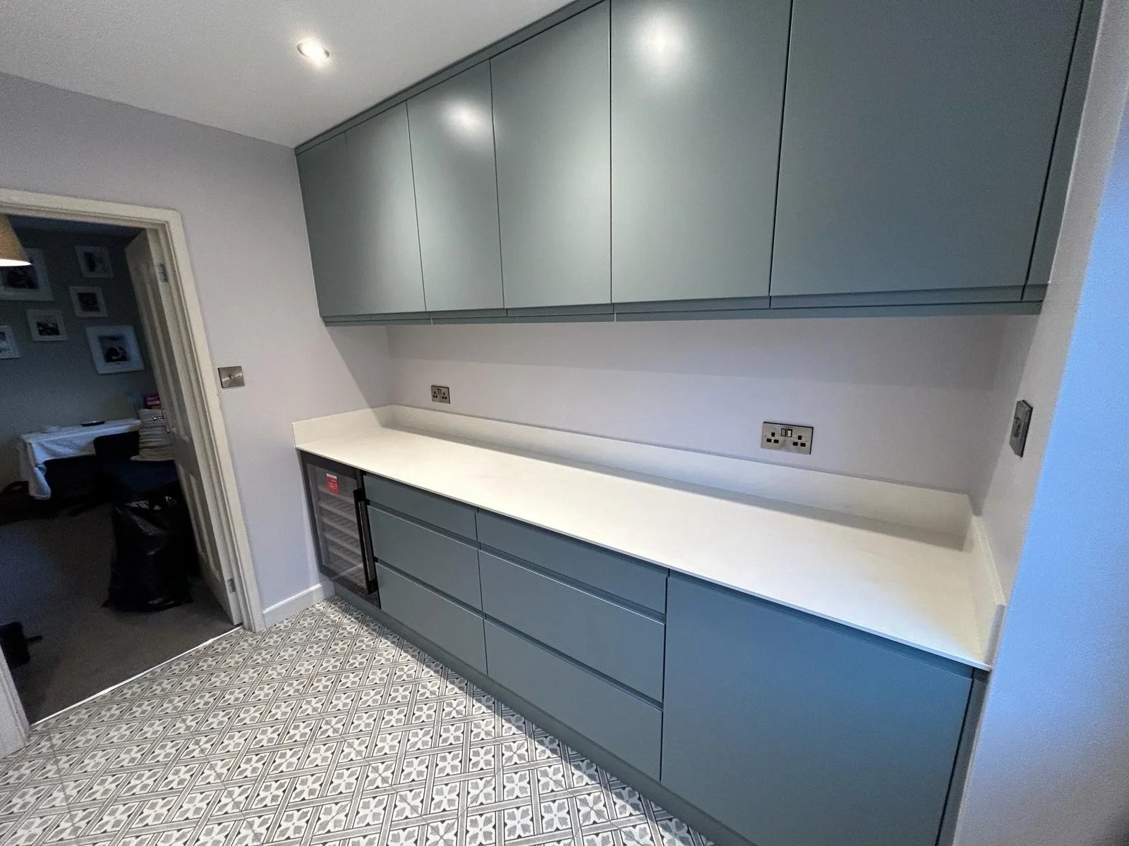 Modern kitchen with grey cabinets, white countertop and patterned floor tiles.