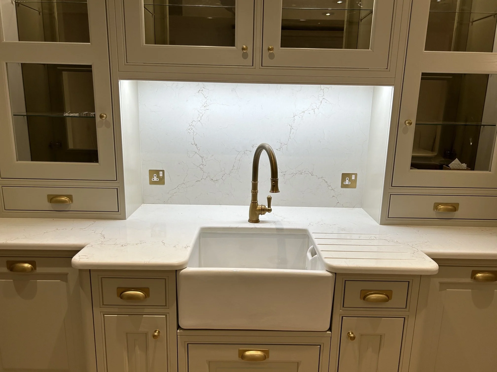 Traditonal kitchen sink with cream cabinets, granite countertop, and a gold faucet, set against a granite backsplash with electrical outlets on each side.