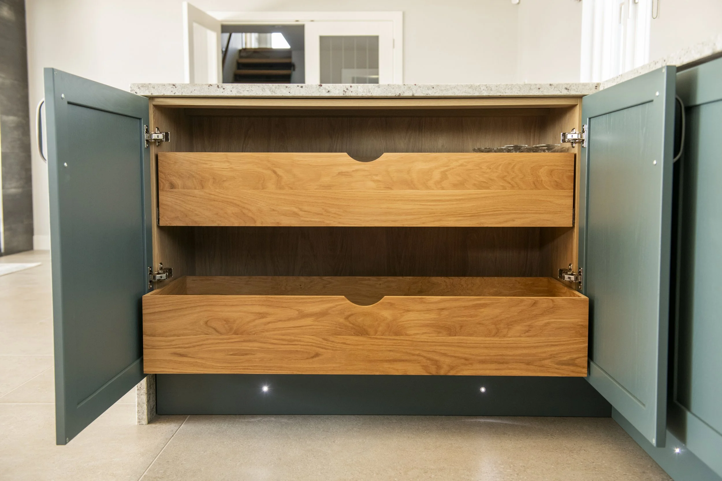 Open kitchen cabinet with two shelves and a countertop above, showing interior wood finish and a sliding drawer at the bottom.