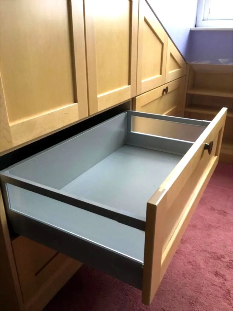 Open drawer with grey interior, wooden cabinetry, and a rug with a reddish hue in the background.