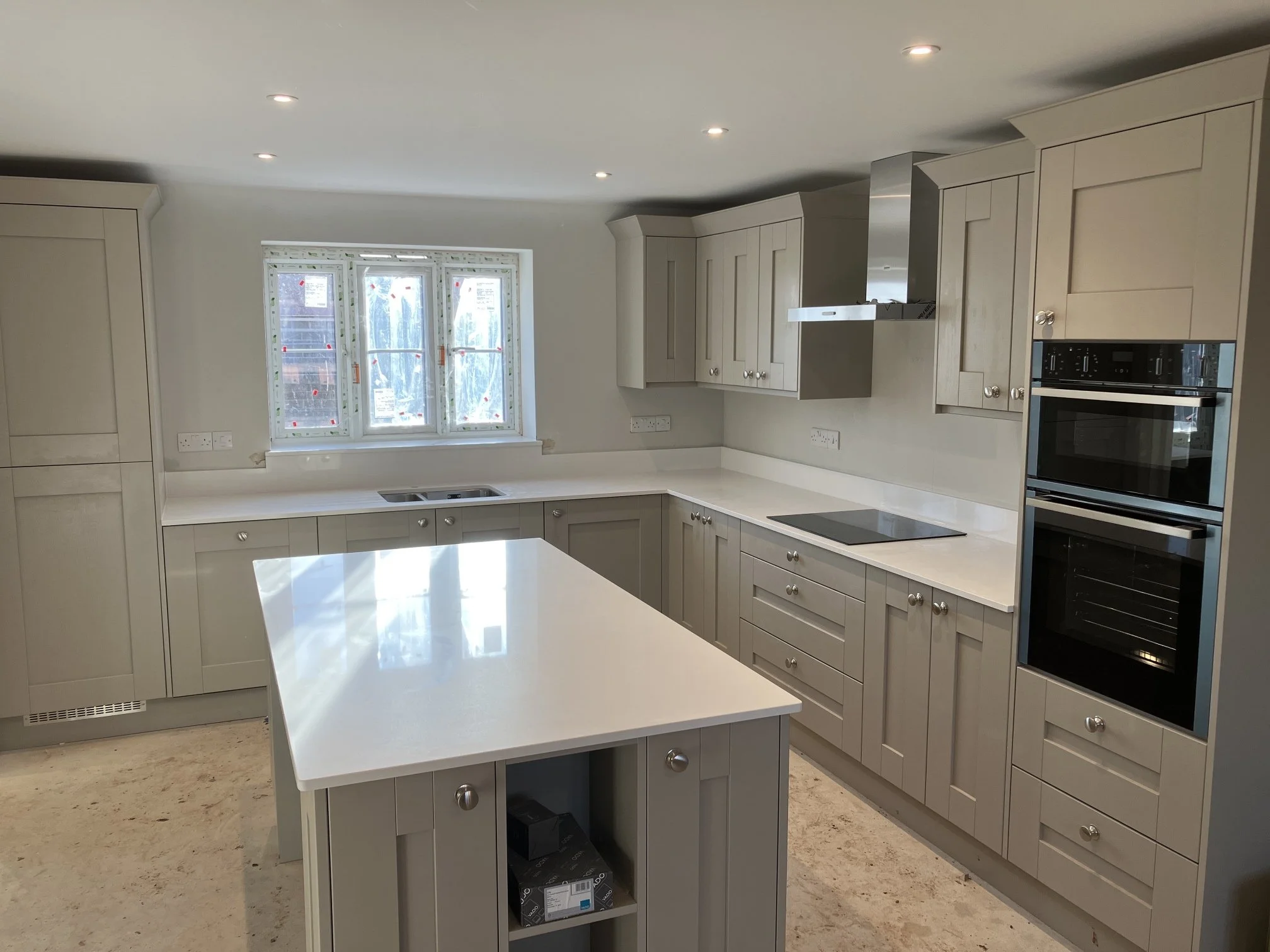 Kitchen with cream-colored cabinets, a white island, a window, and a built-in oven and microwave.