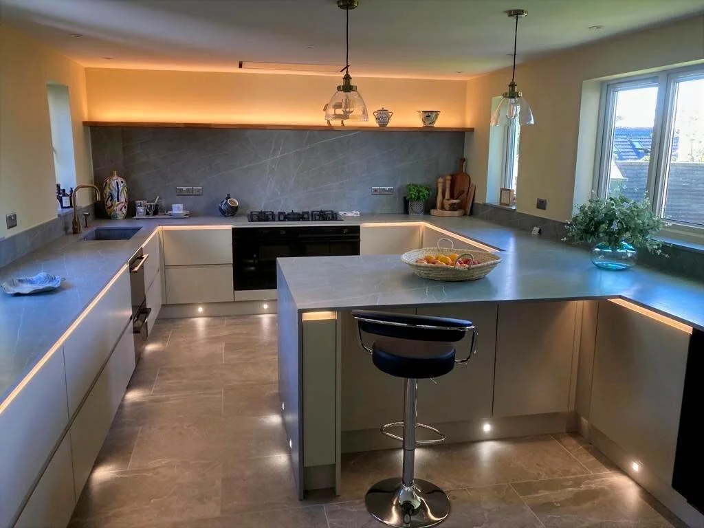Modern grey kitchen featuring an island with floor lighting, a bar stool and decorative items include vases, bowls, and plants.