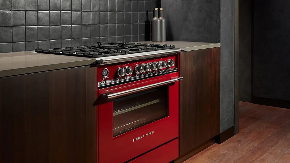 A modern kitchen with a red Fisher & Paykel stove and oven, dark tiled backsplash, dark wooden cabinets, two decorative bottles, and a wood floor.