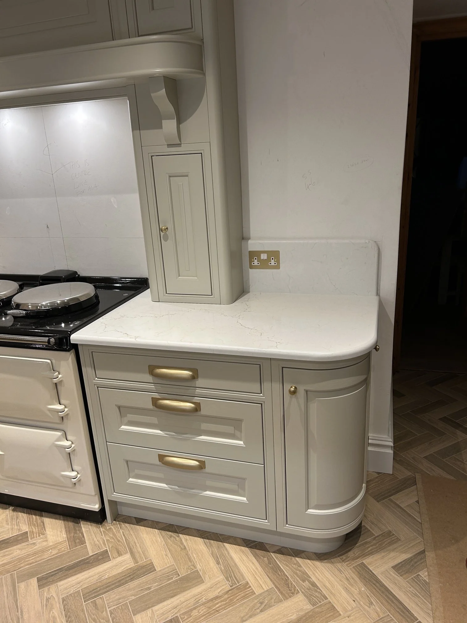 Cream-colored kitchen countertop with gold handles on drawers and a small cabinet, situated next to a vintage cream-colored aga.