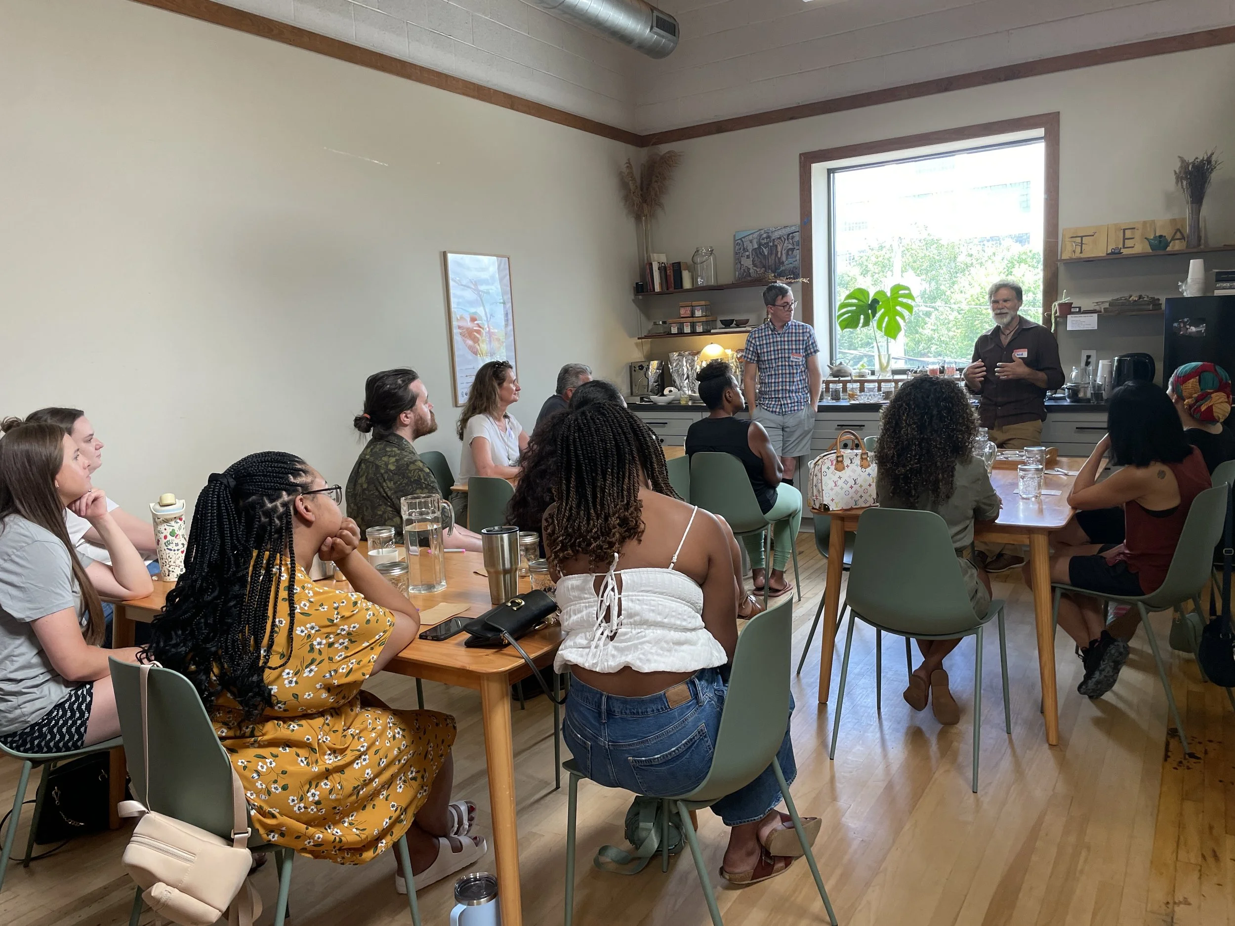 A group of people attending a presentation in a bright, airy room with large windows and decorated with plants and artwork.
