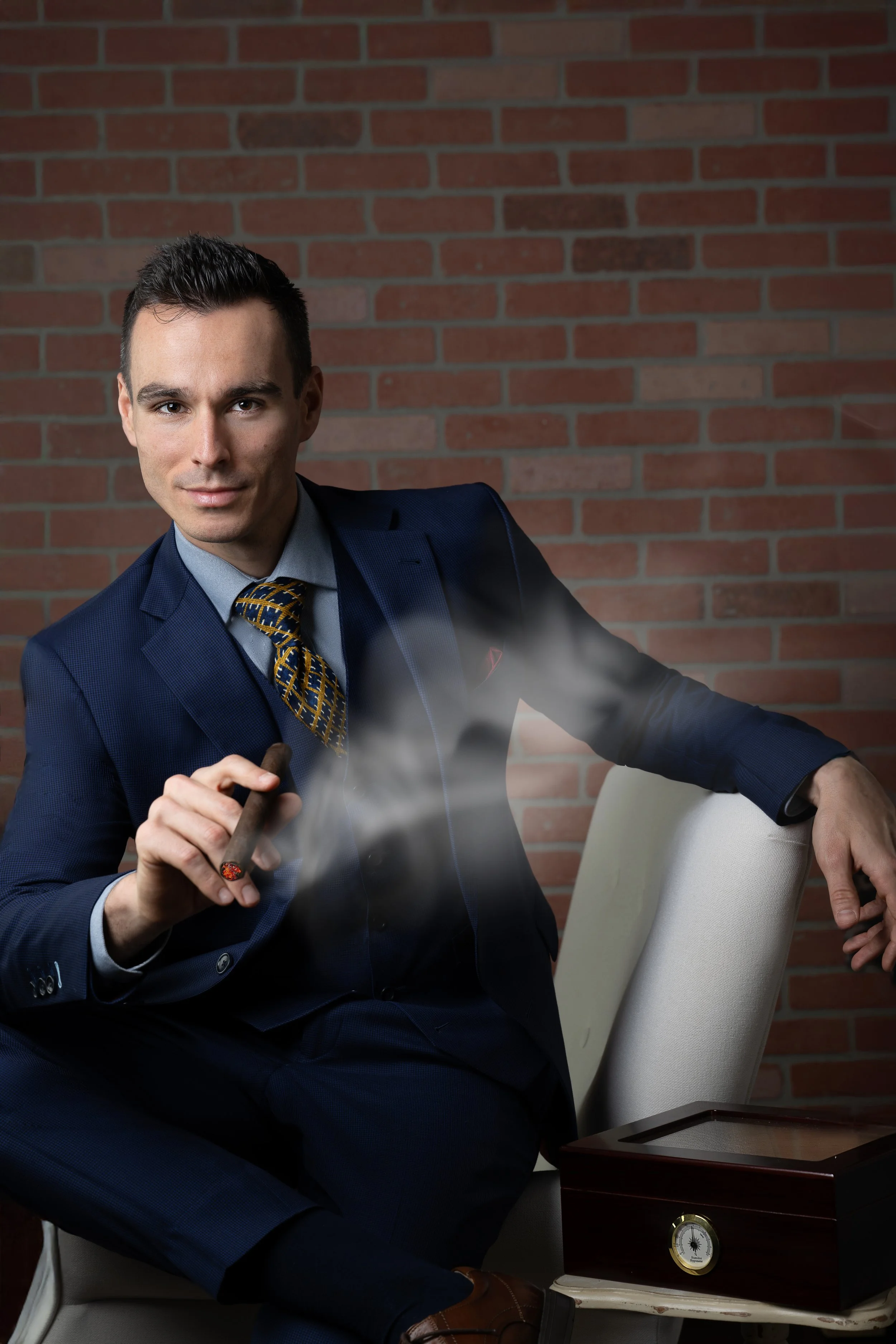 Man in suit against brick wall smoking a cigar