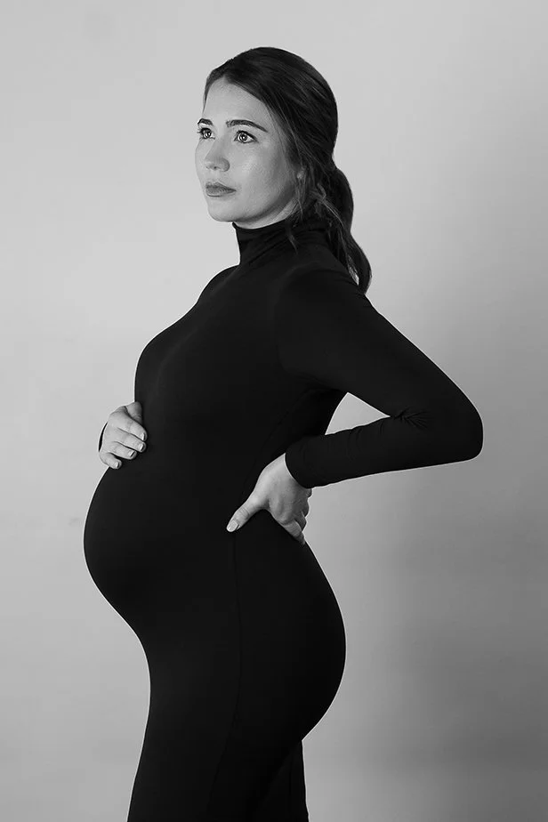 Black and white photo of a pregnant woman wearing an all black slim fitting dress.
