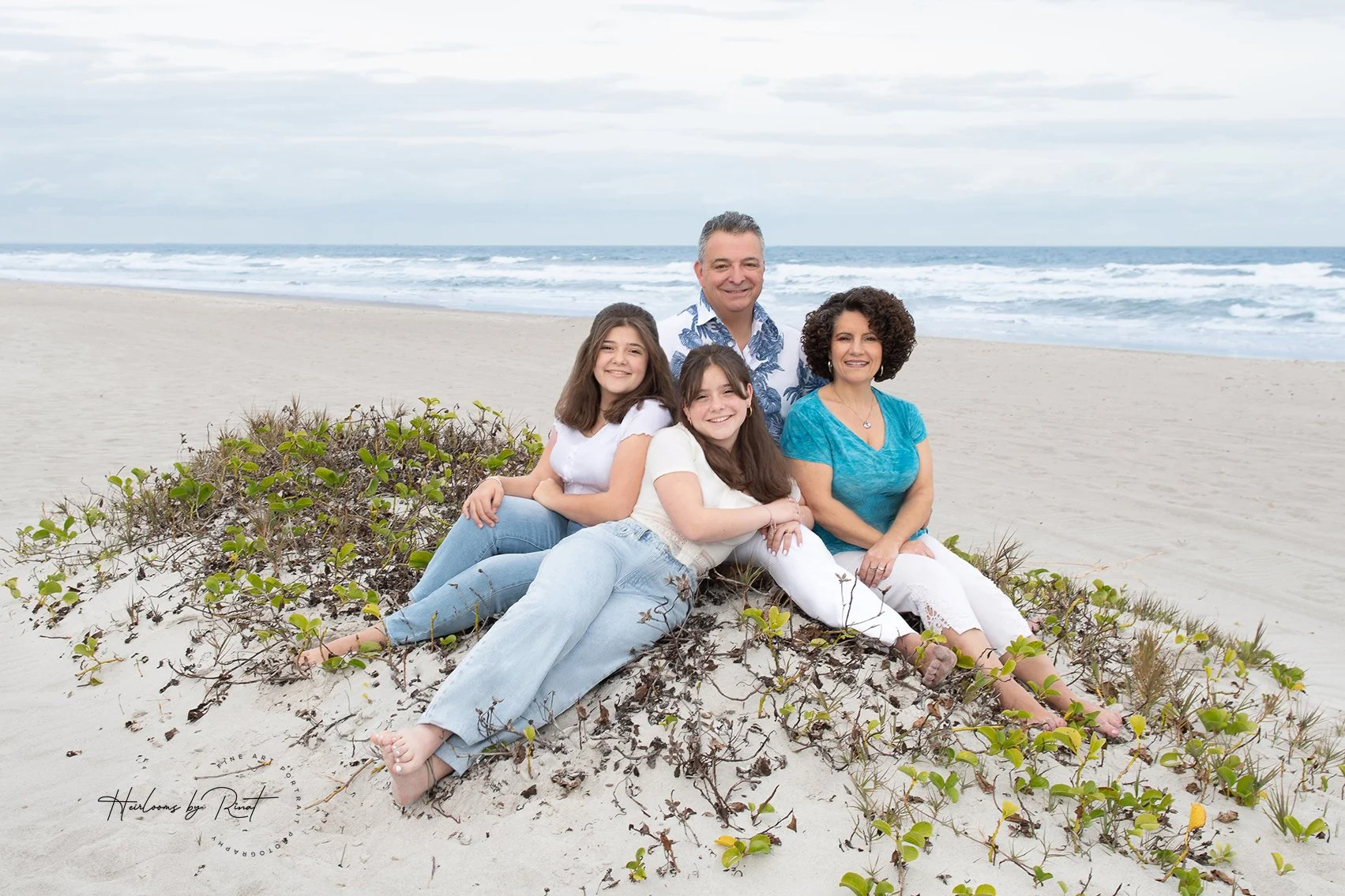 Family by the ocean parents with 2 daughters on sandy mound on beach