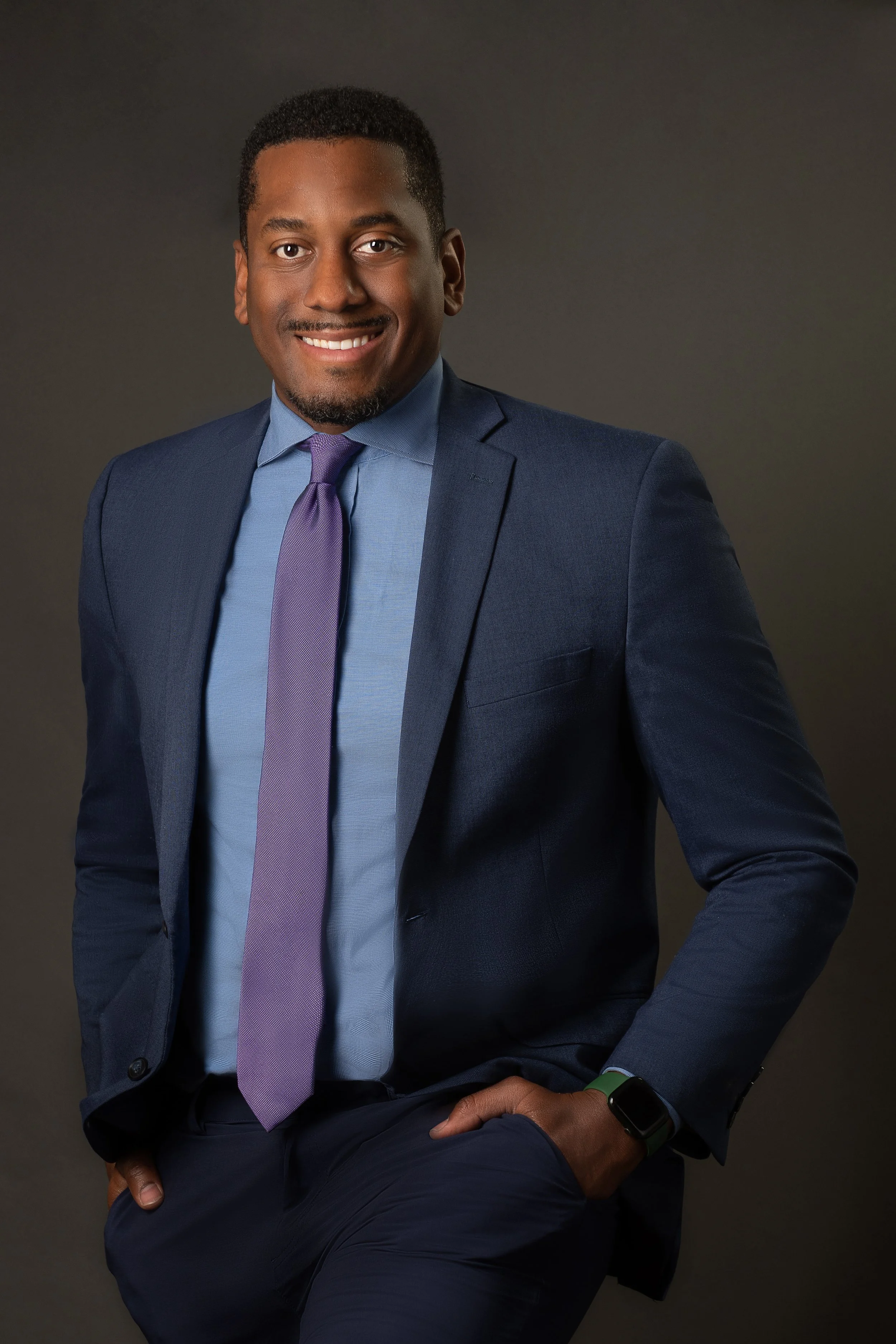 Business Man in suit with a purple tie against grey background standing in studio
