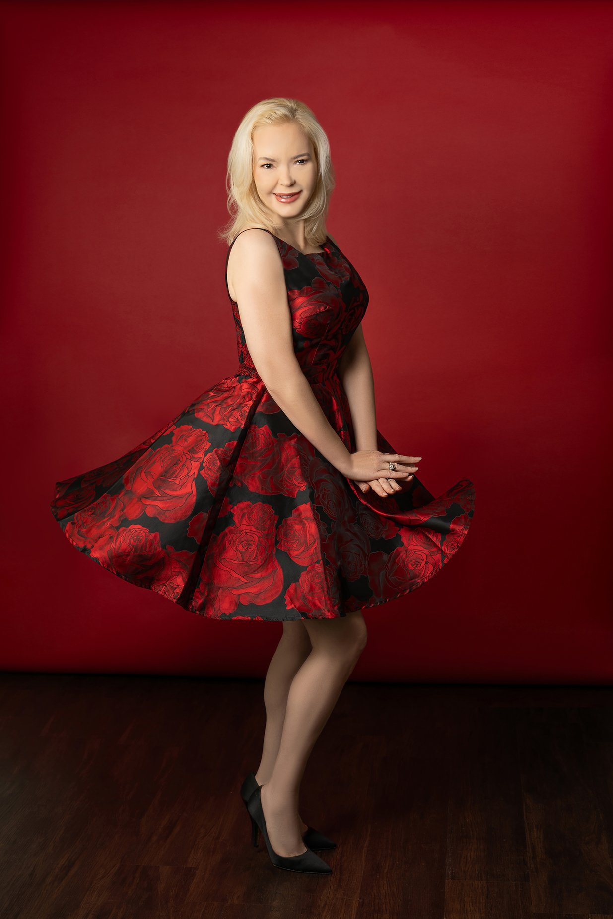 Blonde woman twirling in red and black rose patterned dress.