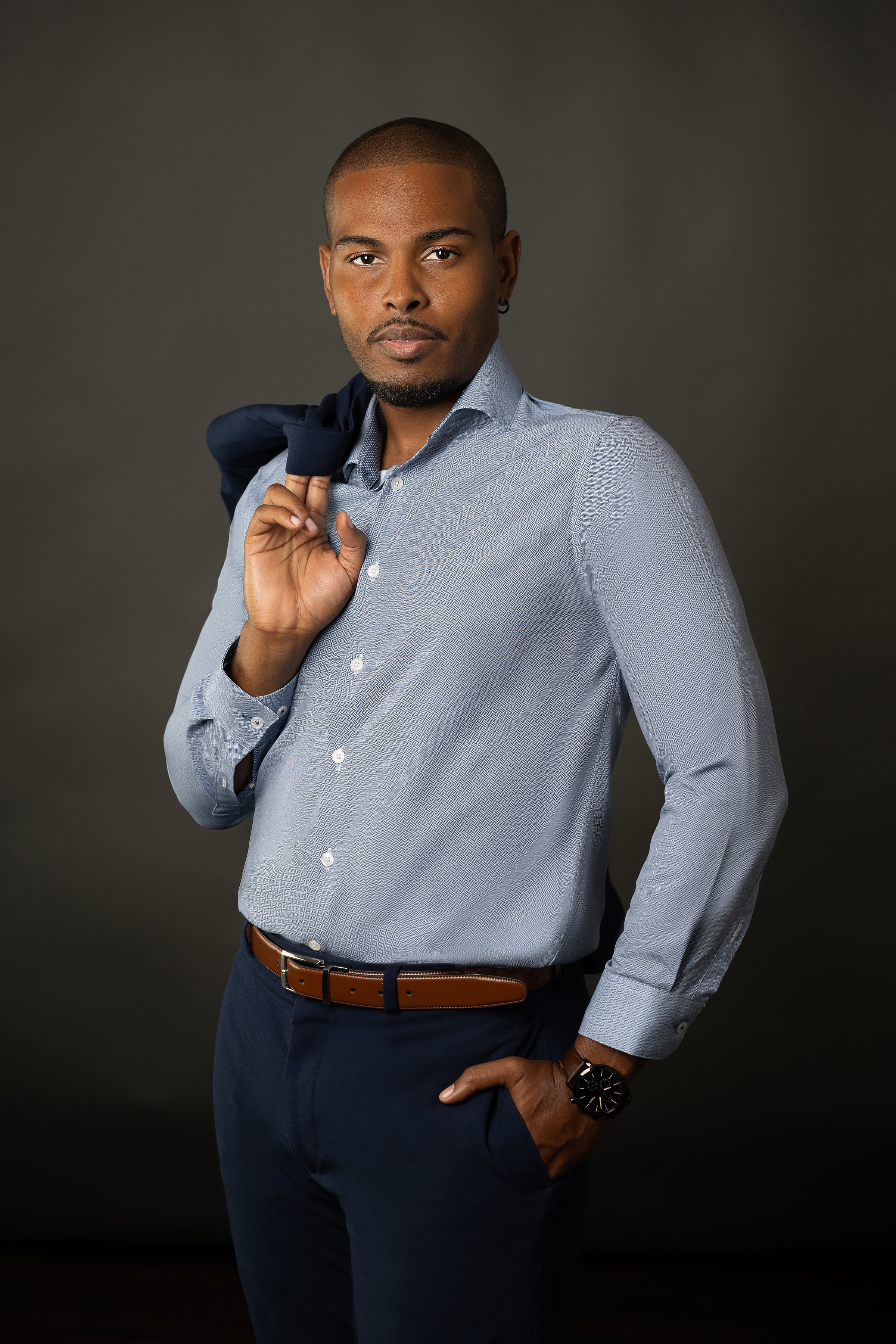 African American man in a blue dress shirt and navy pants with his suit jacket over his shoulder.
