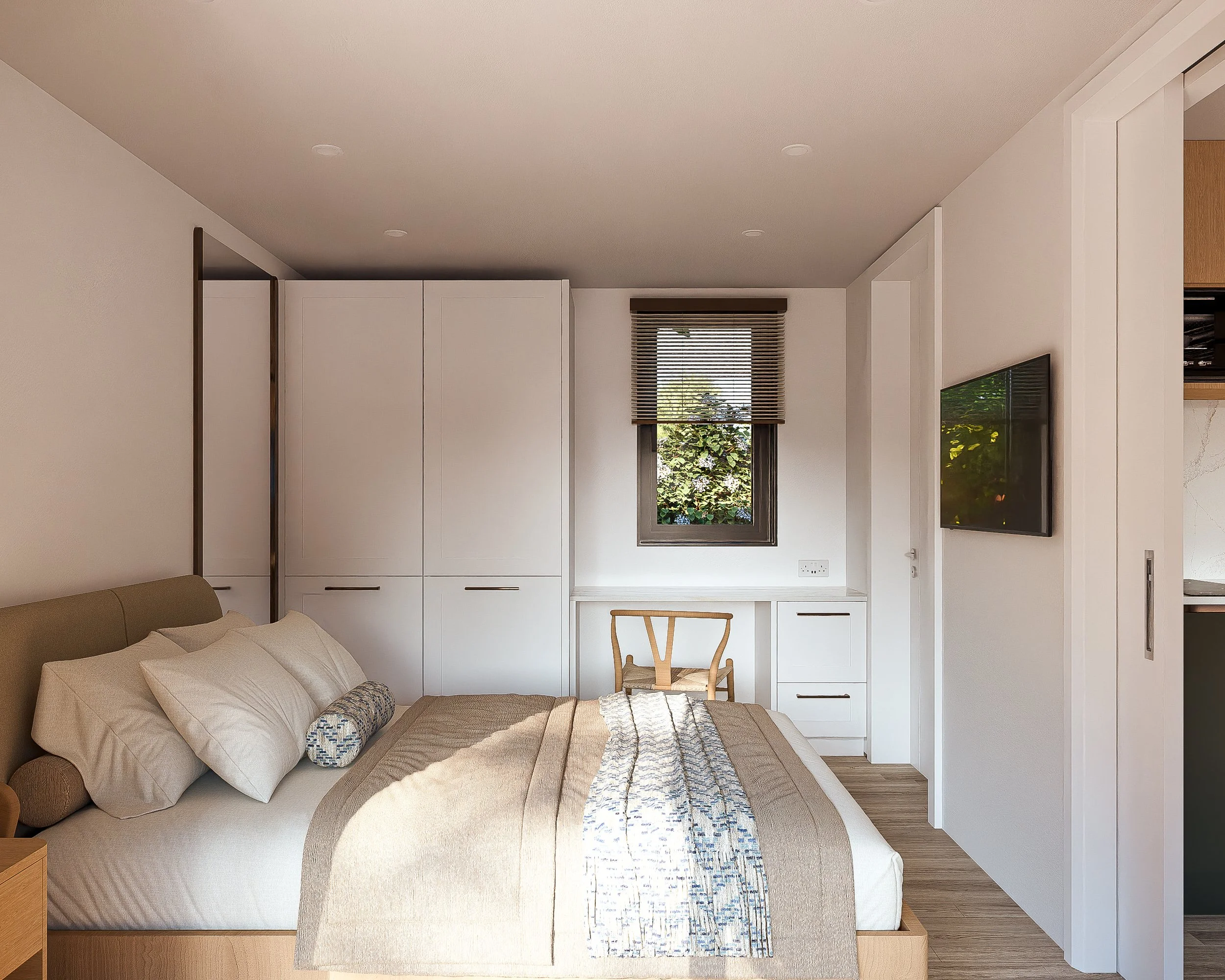 Bauhu hurricane resistant modular hospitality pod Modern bedroom with beige bed, white pillows, a beige blanket, a window with blinds, a small desk and chair, and a flat-screen TV mounted on the wall.