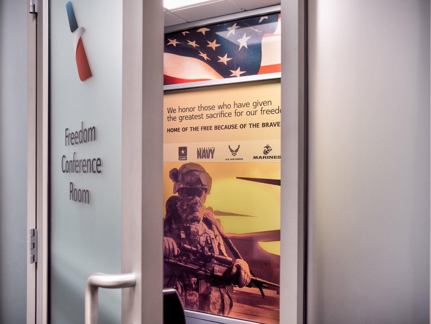 The door to a conference room with a sign labeled 'Freedom Conference Room' and a mural celebrating American military service, featuring the U.S. flag, a soldier in uniform, and logos of Navy, Air Force, and Marines.