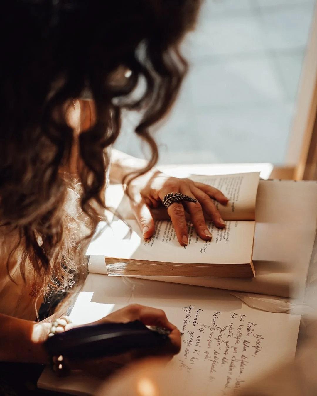 Person with curly hair writing on paper at a table with sunlight shining on them.