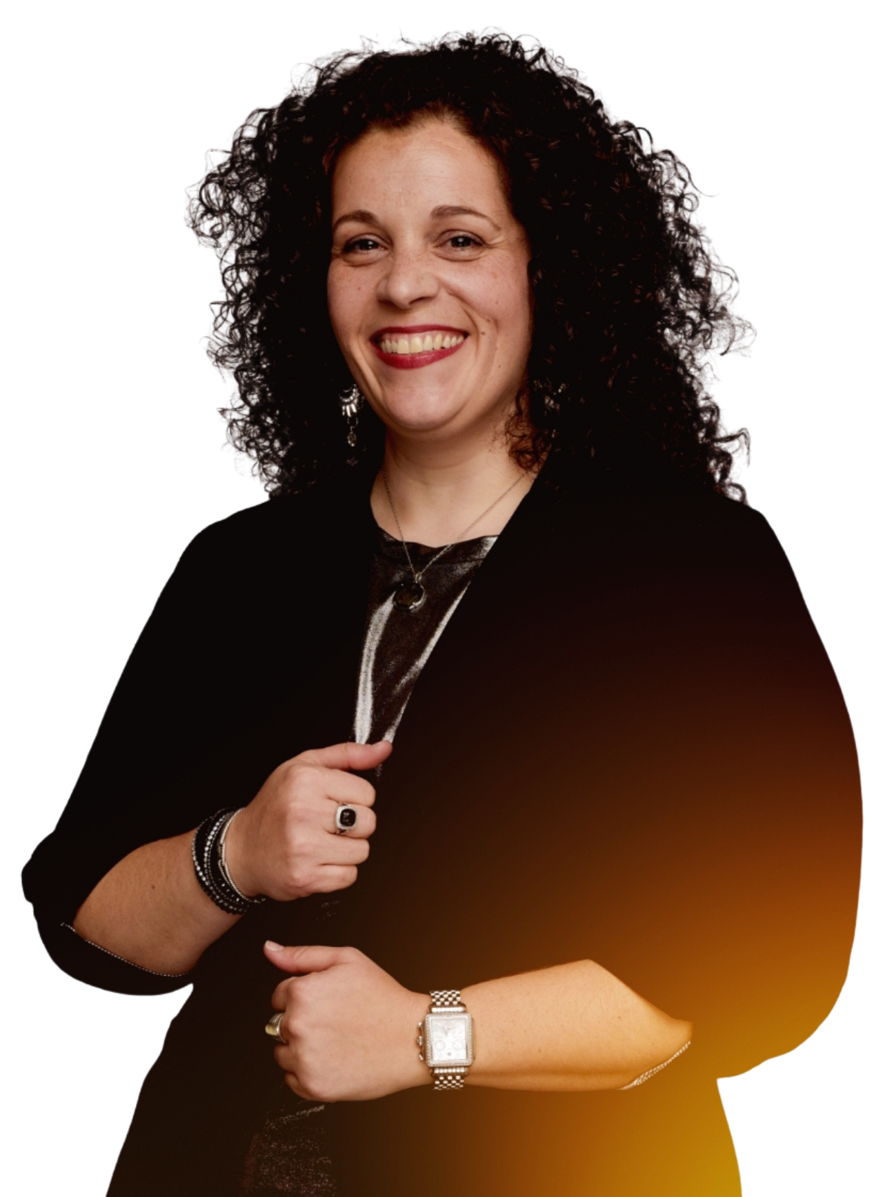 A woman with curly brown hair smiling, wearing a black jacket, jewelry, and a watch, posing against a plain white background.