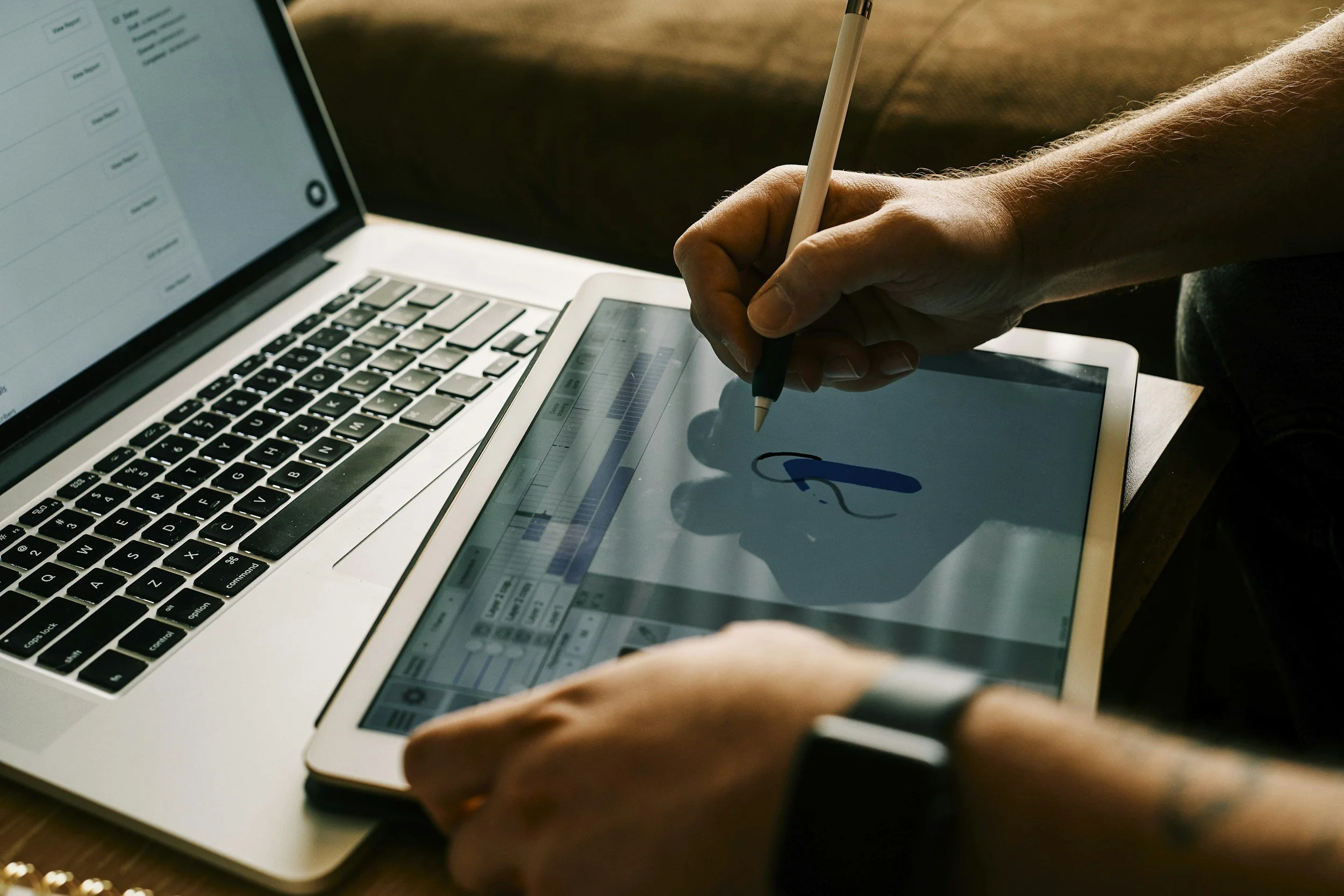 Person using a stylus to draw or write on a tablet while a laptop is open nearby.