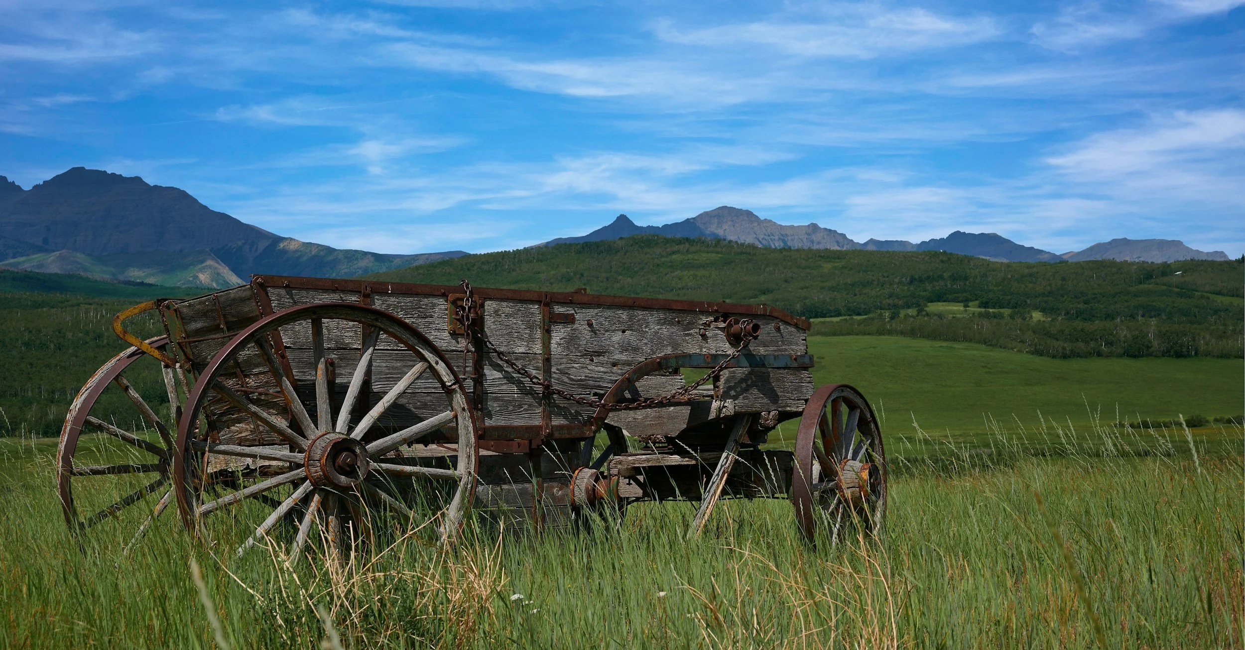 Old ranch wagon in Alberta foothills with the Rocky Mountains behind, typical of farms and ranches served by a Canadian virtual assistant