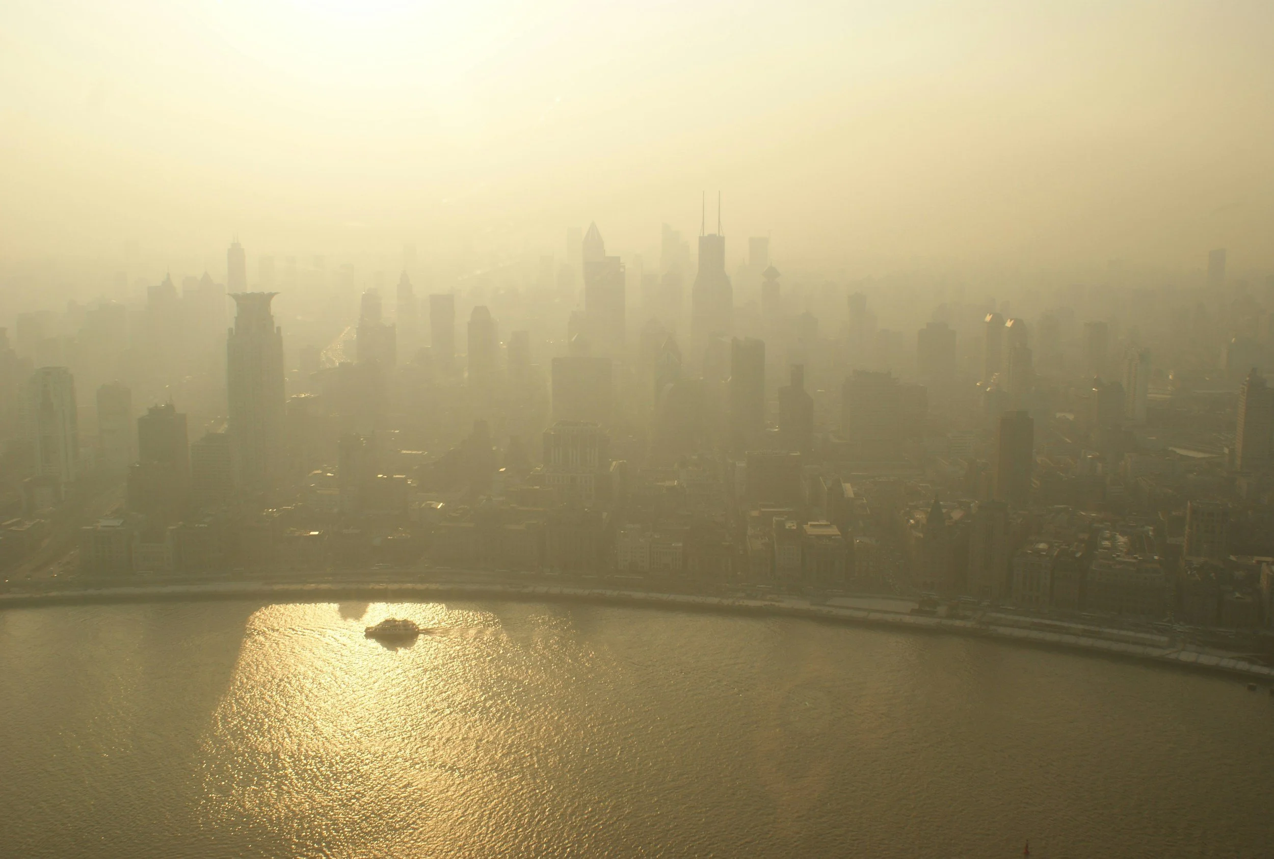 A photo of a city downtown skyline, next to a shining body of water, covered in a thick, yellow haze.