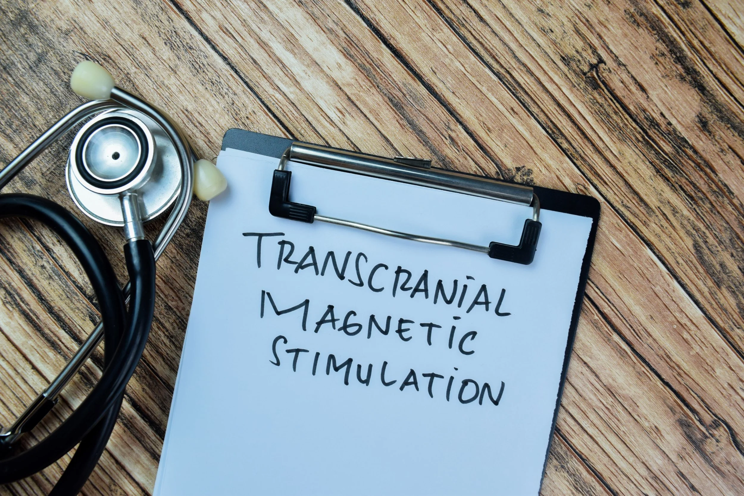 Transcranial Magnetic Stimulation written on a clipboard alongside a stethoscope