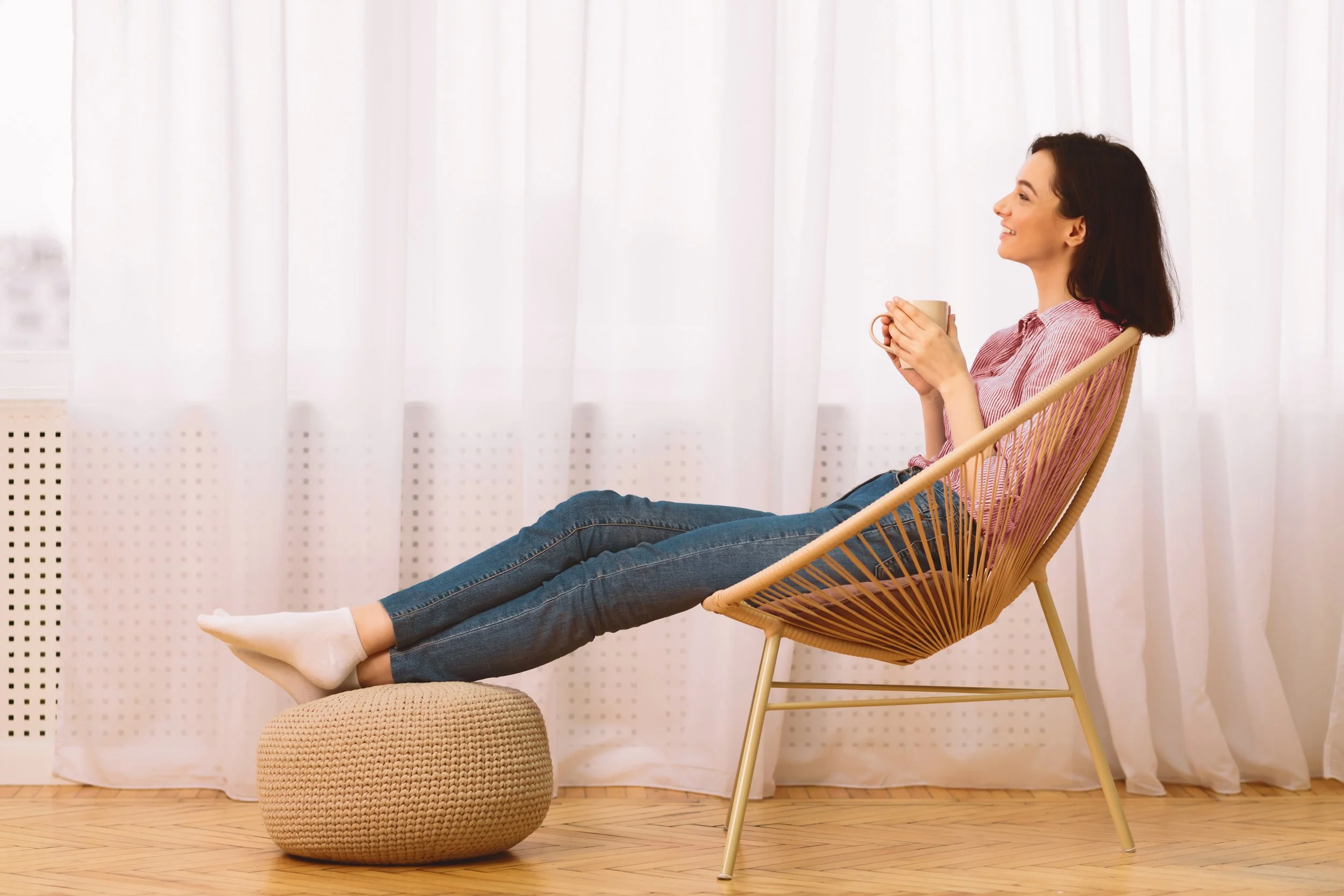 A woman relaxing by white curtains in her home