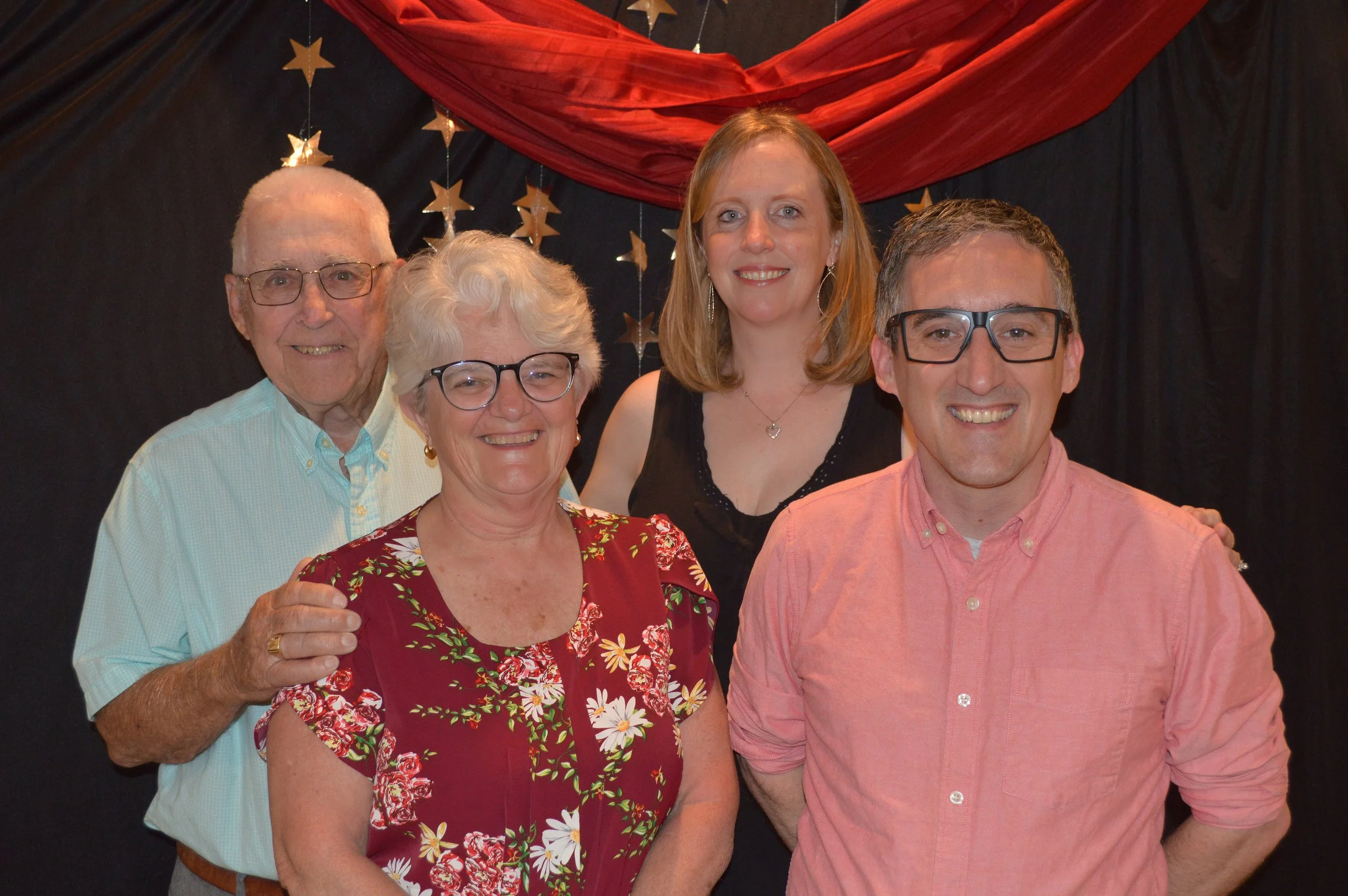 Group of five people smiling, standing in front of a decorative backdrop with stars and red fabric.