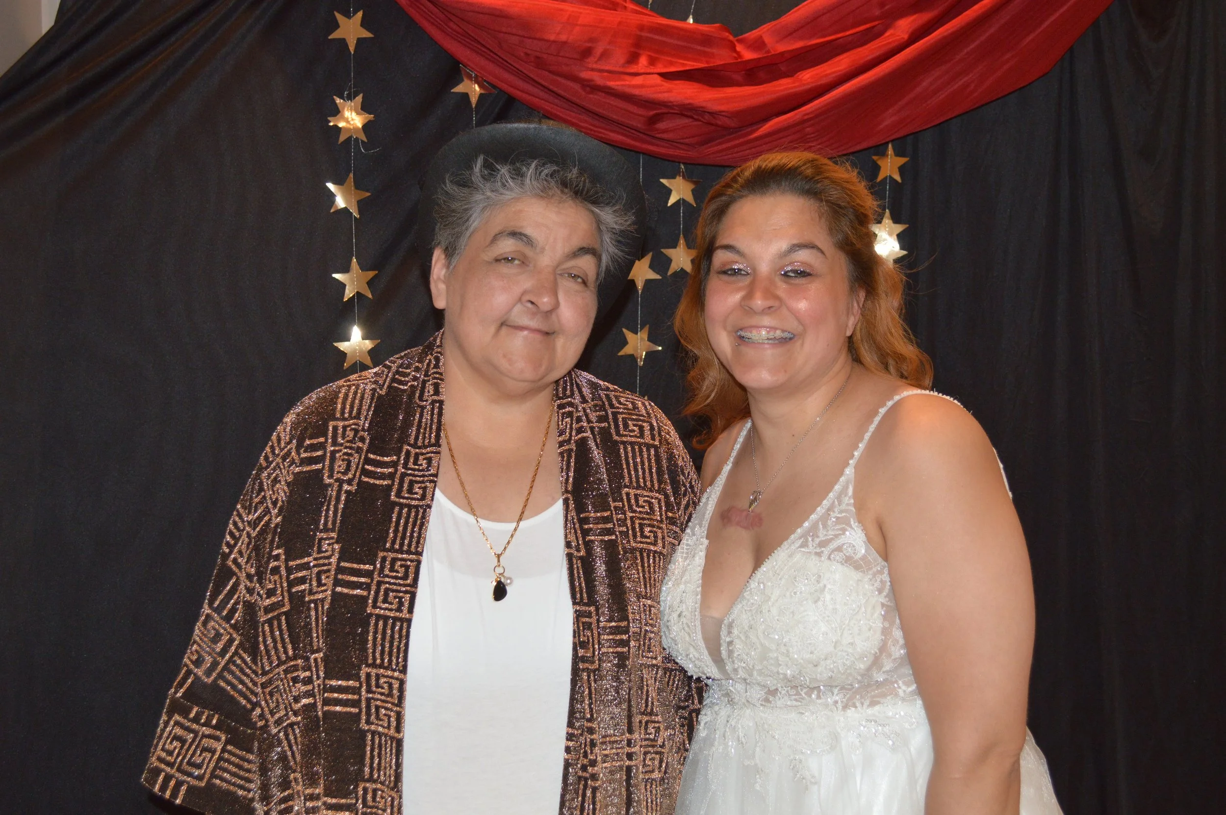 Two women smiling in front of a black background decorated with gold stars and red fabric.