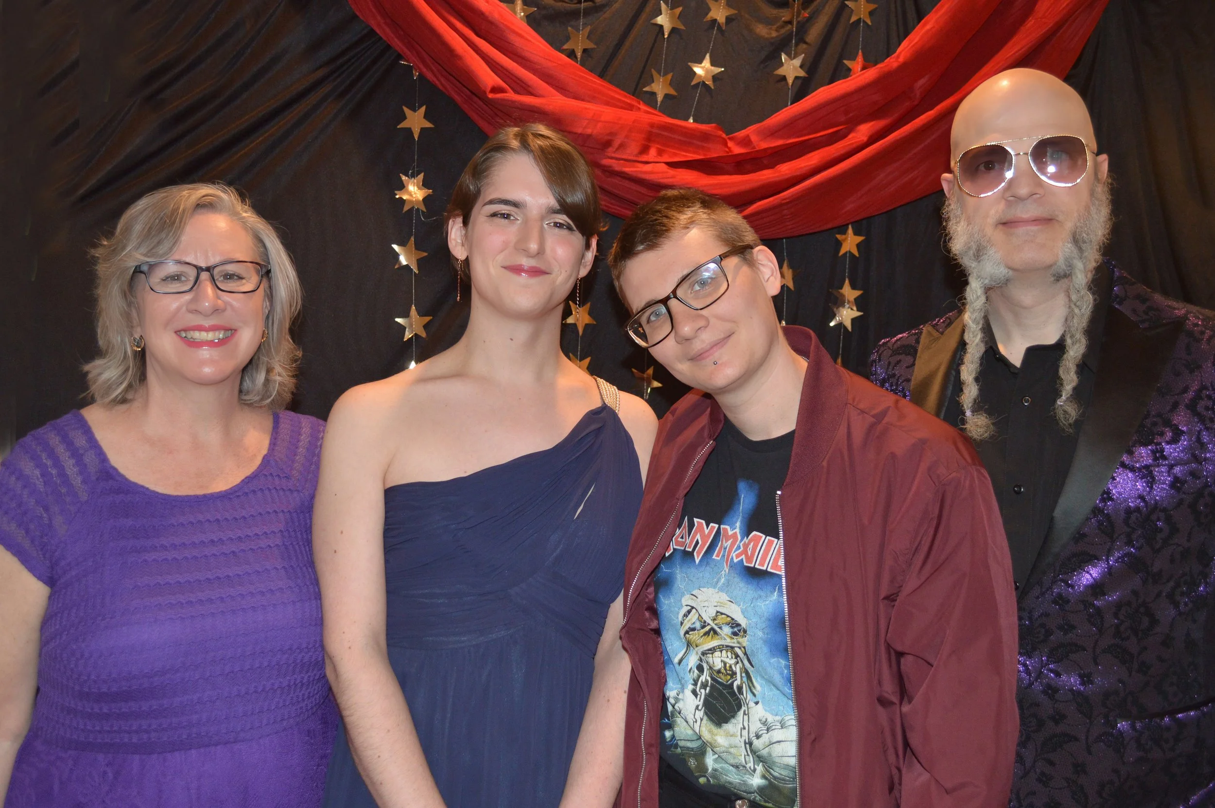 Group of five people standing in front of a black background decorated with red fabric and gold star hanging ornaments.