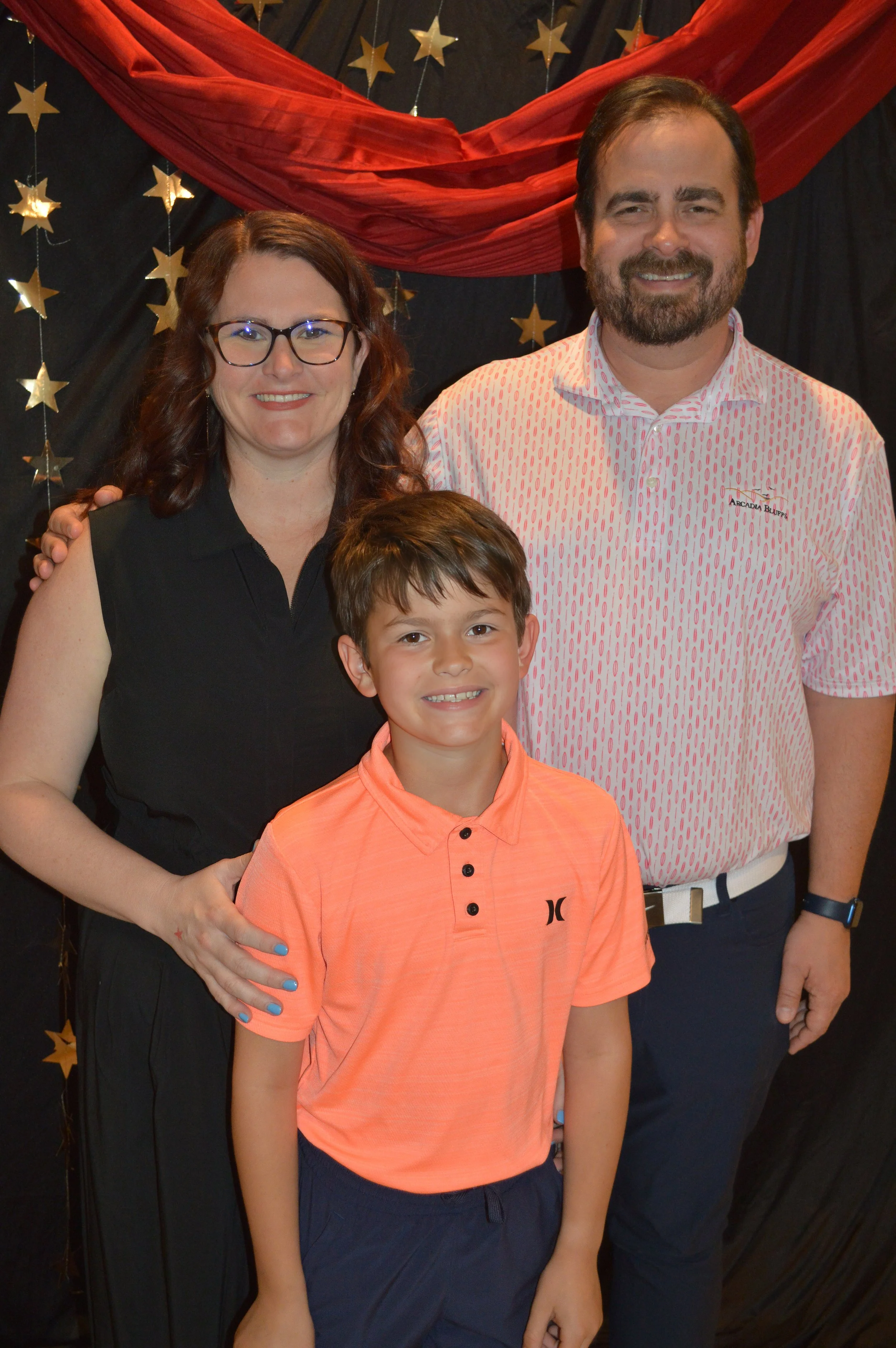 A woman, a man, and a boy smiling for a photo in front of a star and red drapery backdrop at an event.