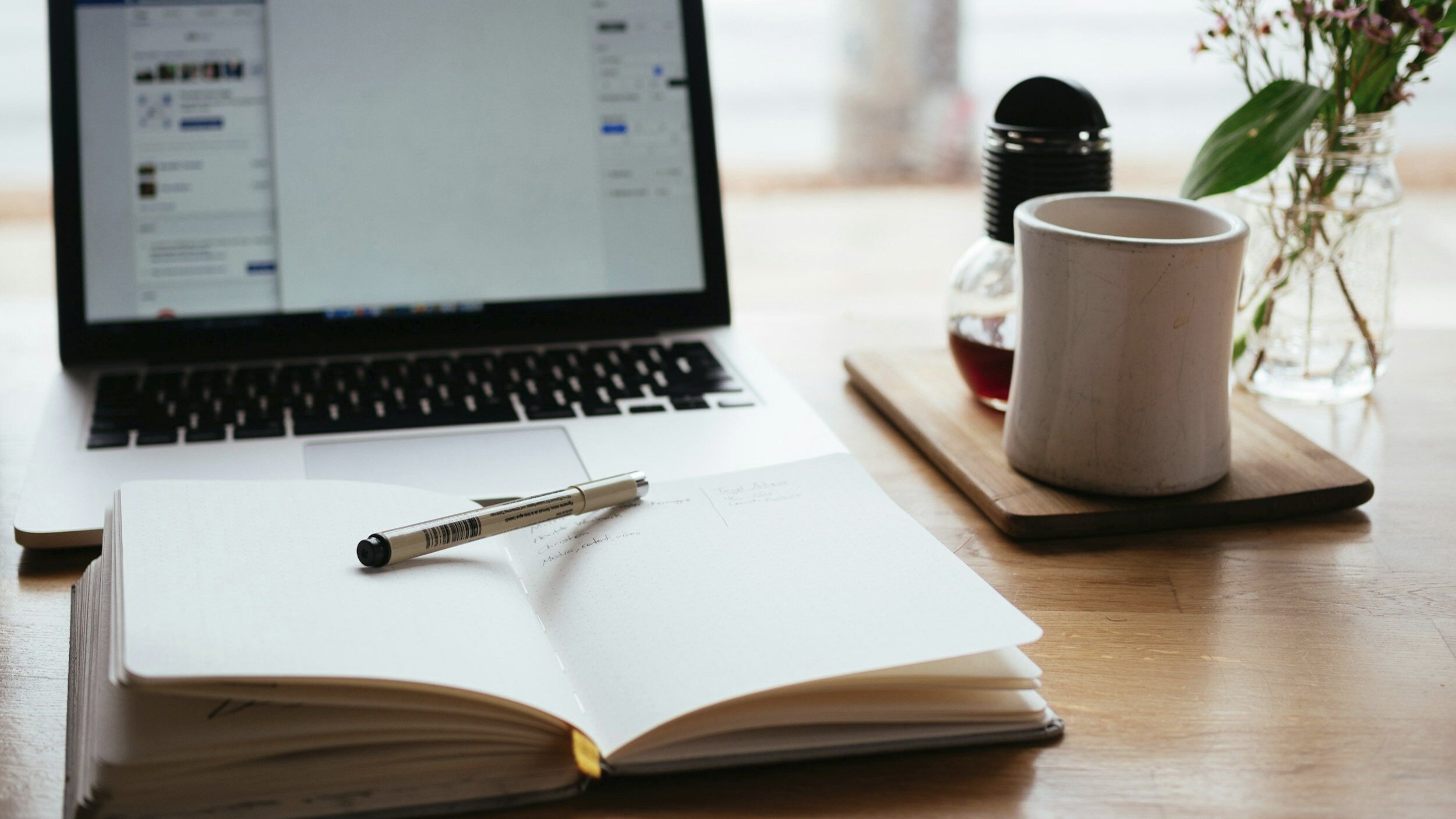 Image of a laptop, cup of coffe, and organizer open on a table illustrating the start of an online business coaching session.