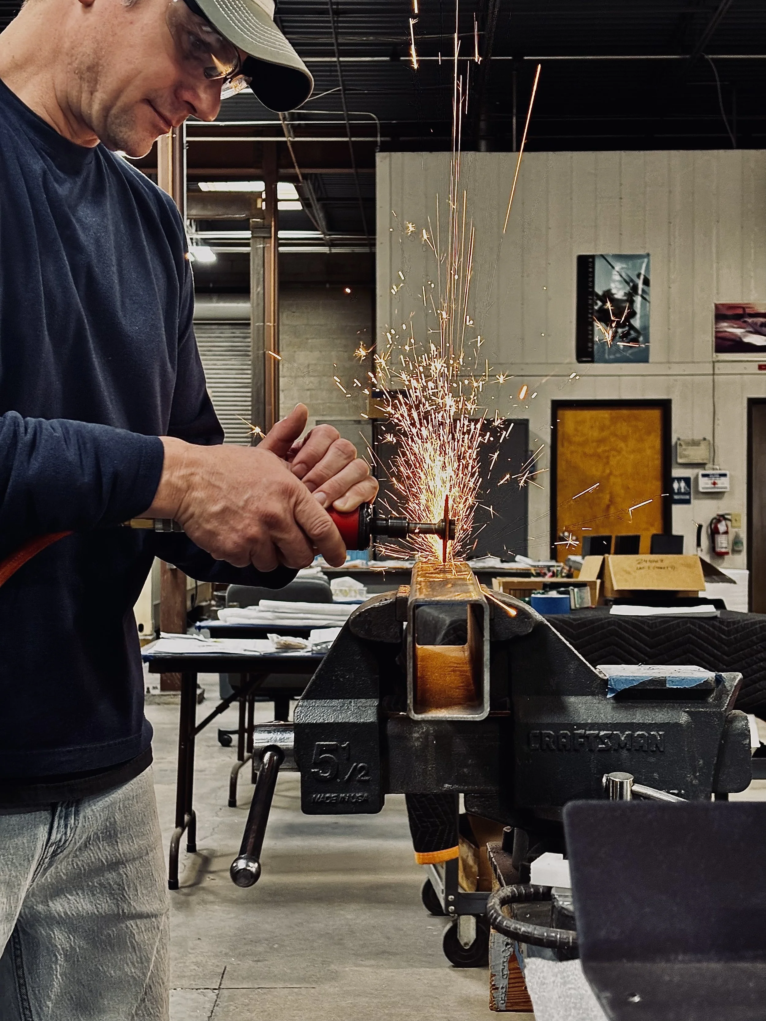 A man is grinding metal on a workbench in a workshop, with sparks flying as he uses a handheld rotary tool.